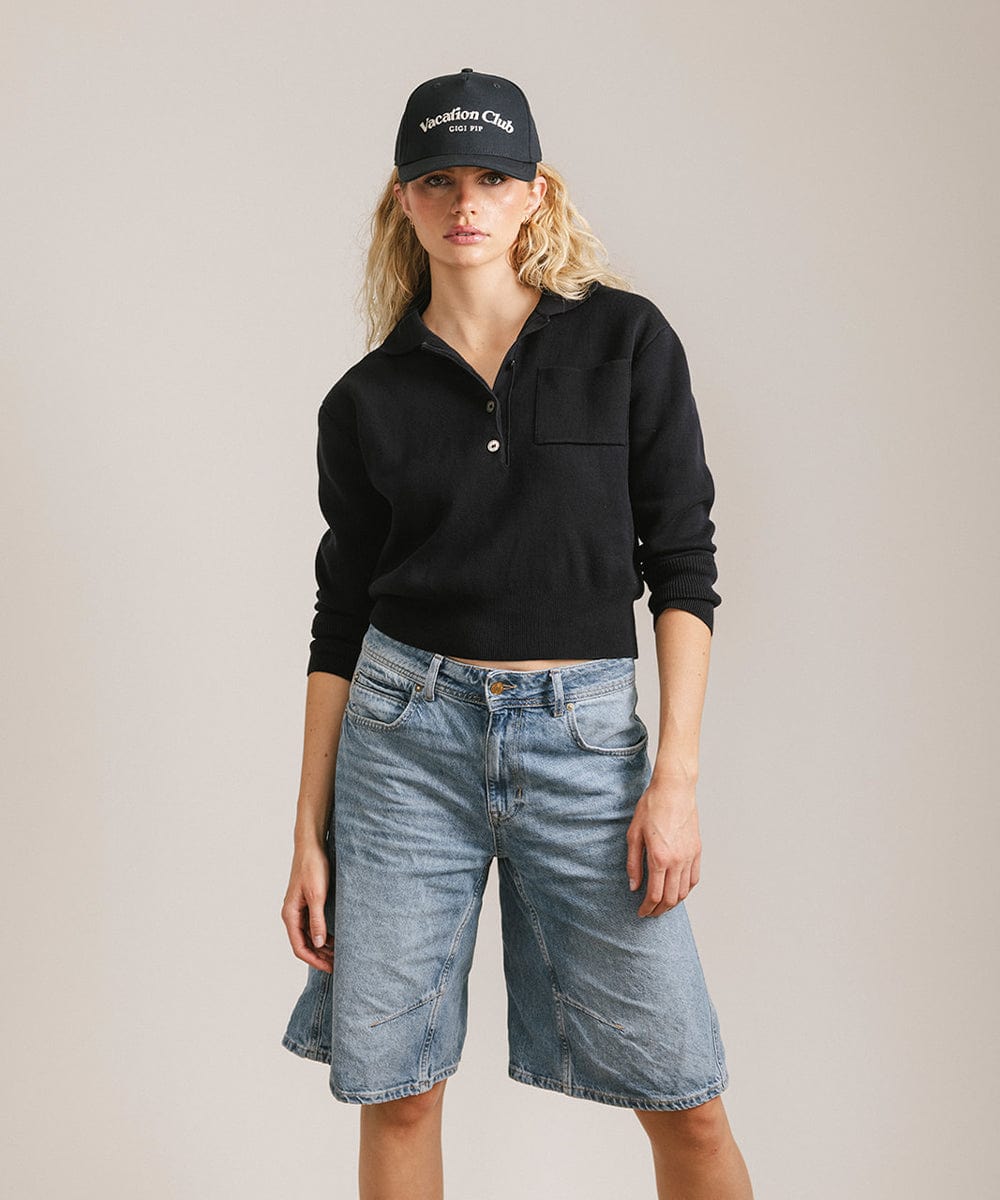 Woman wearing a navy cap with 'Vacation Club' text, a black shirt and denim shorts against a plain background #color_navy