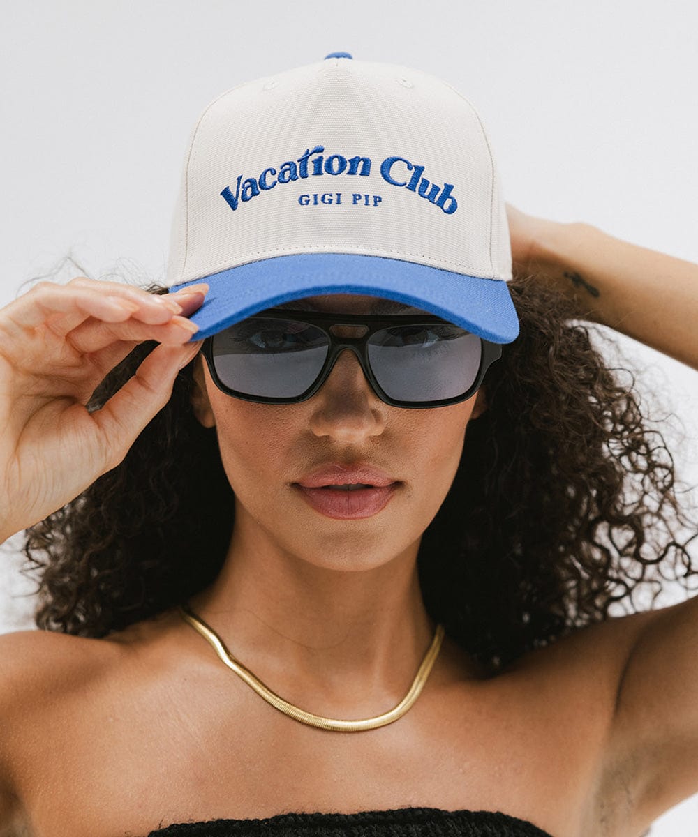Woman wearing a cream and blue cap with 'Vacation Club' text, sunglasses and a gold chain against a plain background #color_cream - blue