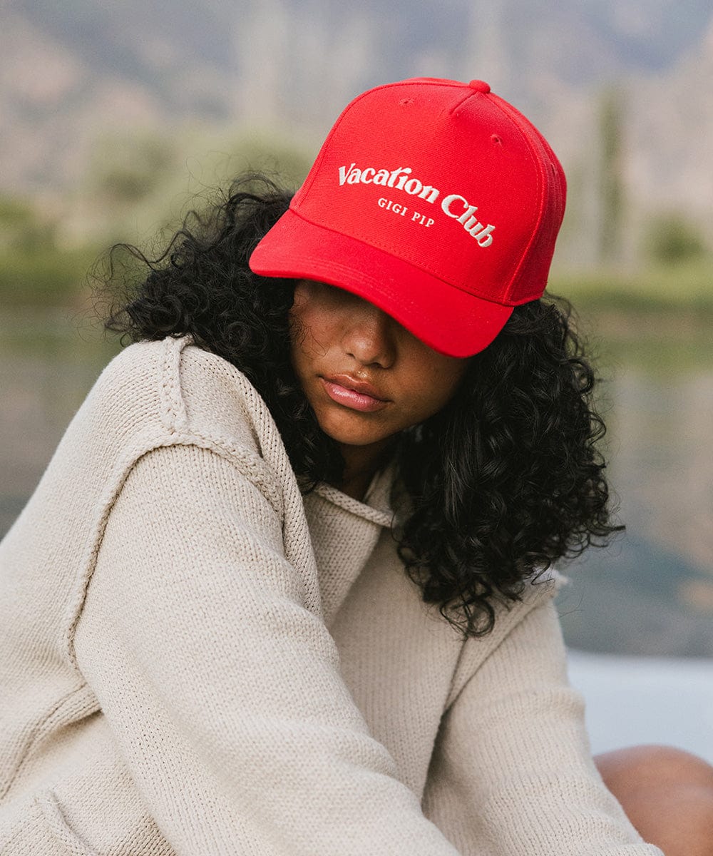 Woman wearing a red cap with 'Vacation Club' text and a white sweater, posing against a plain background #color_red