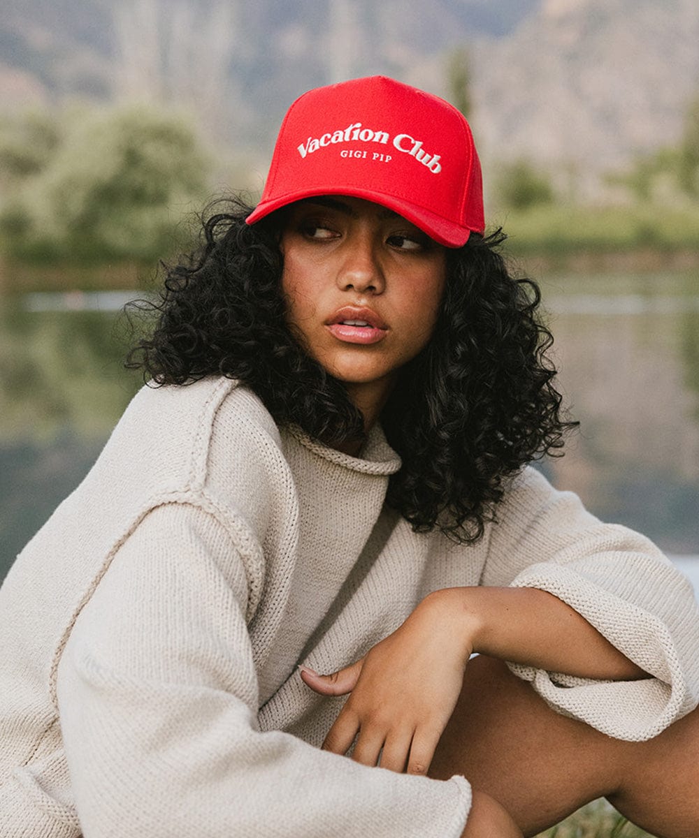 Woman wearing a red cap with 'Vacation Club' text and a white sweater, posing against a plain background #color_red