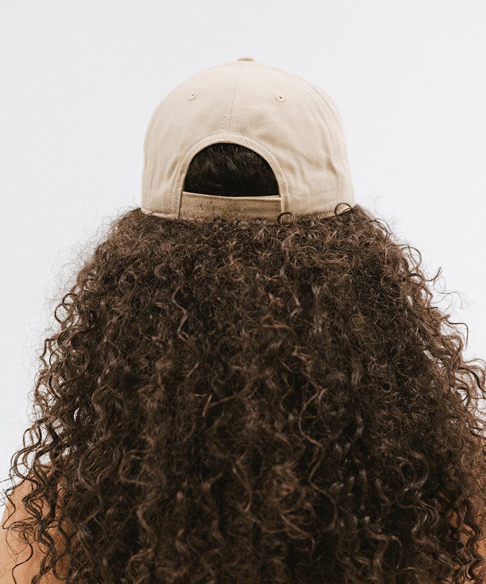Woman with curly hair wearing a tan cap against a plain background #color_tan