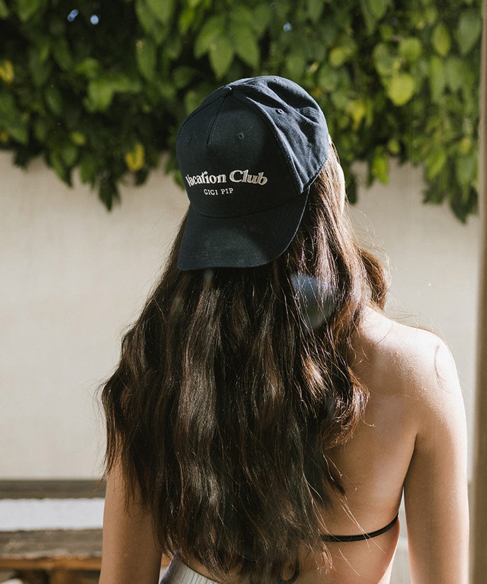 Woman with long hair wearing a navy cap against a background with leaves #color_navy