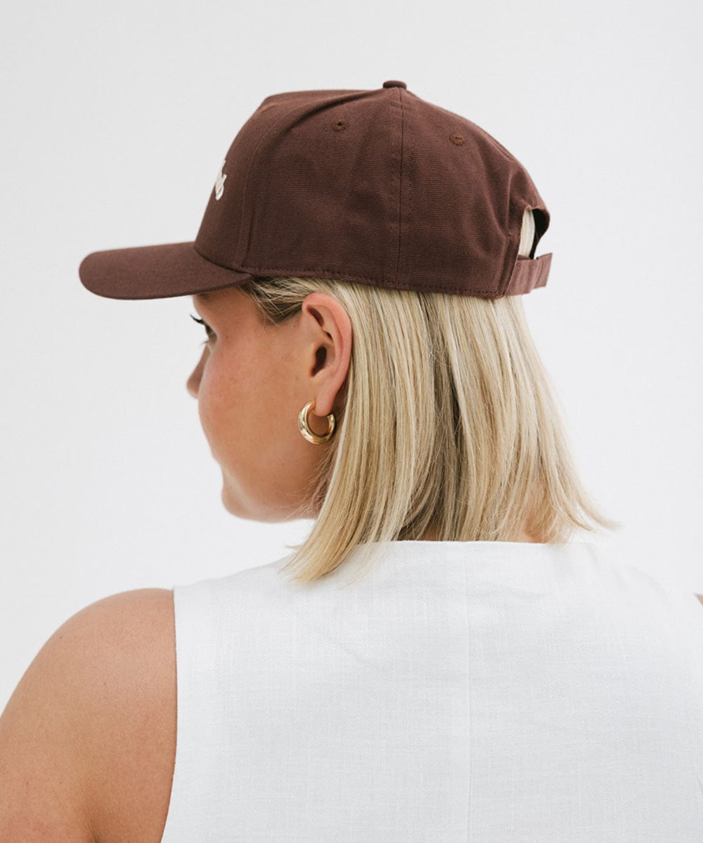 Woman wearing a chocolate brown colored cap and a white top against a plain background #color_chocolate brown