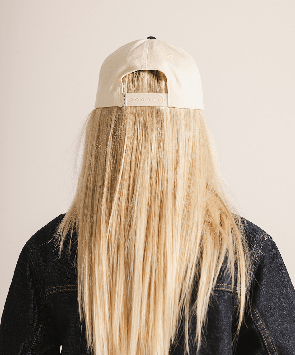 Person wearing a beige cap with a brand logo on a plain background #color_cream - black