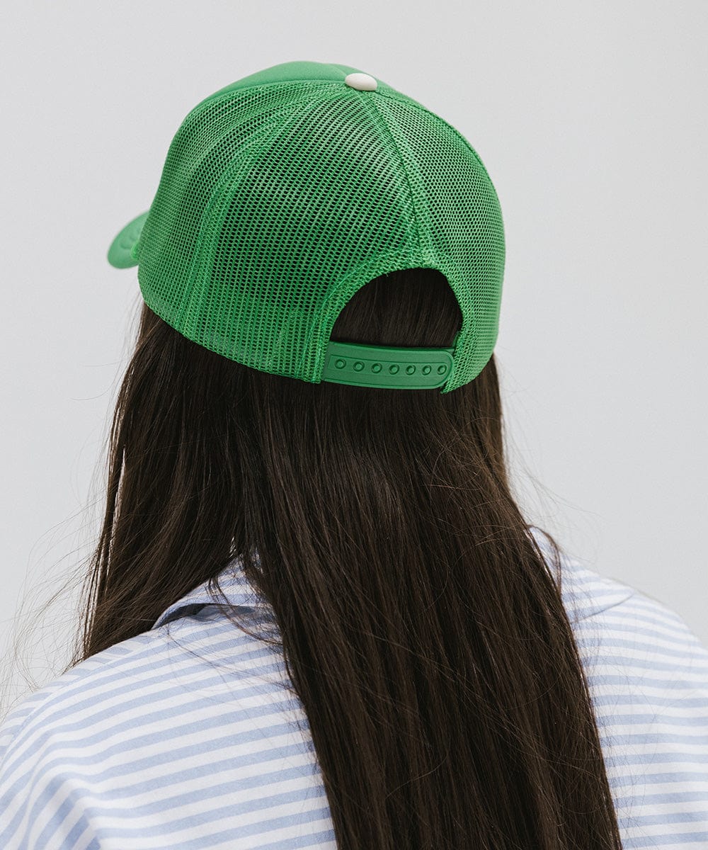 Woman wearing a vintage green colored trucker hat with 'Vintage Goods' text and a white shirt with blue lines, facing behind against a plain background #color_vintage green
