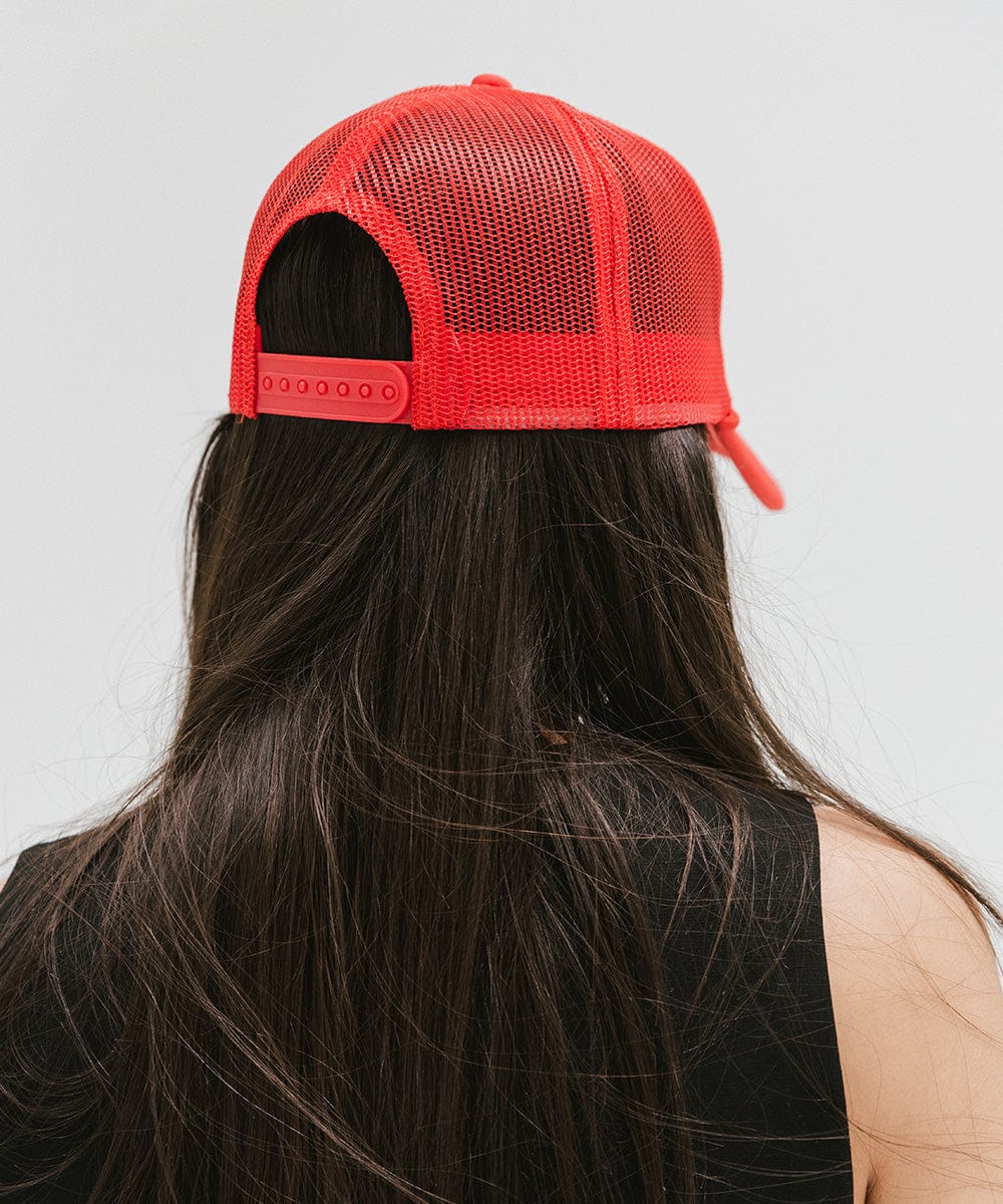 Woman wearing a cream and vintage red colored trucker hat with 'Vintage Goods' text and a black top, facing behind against a plain background #color_cream-vintage red