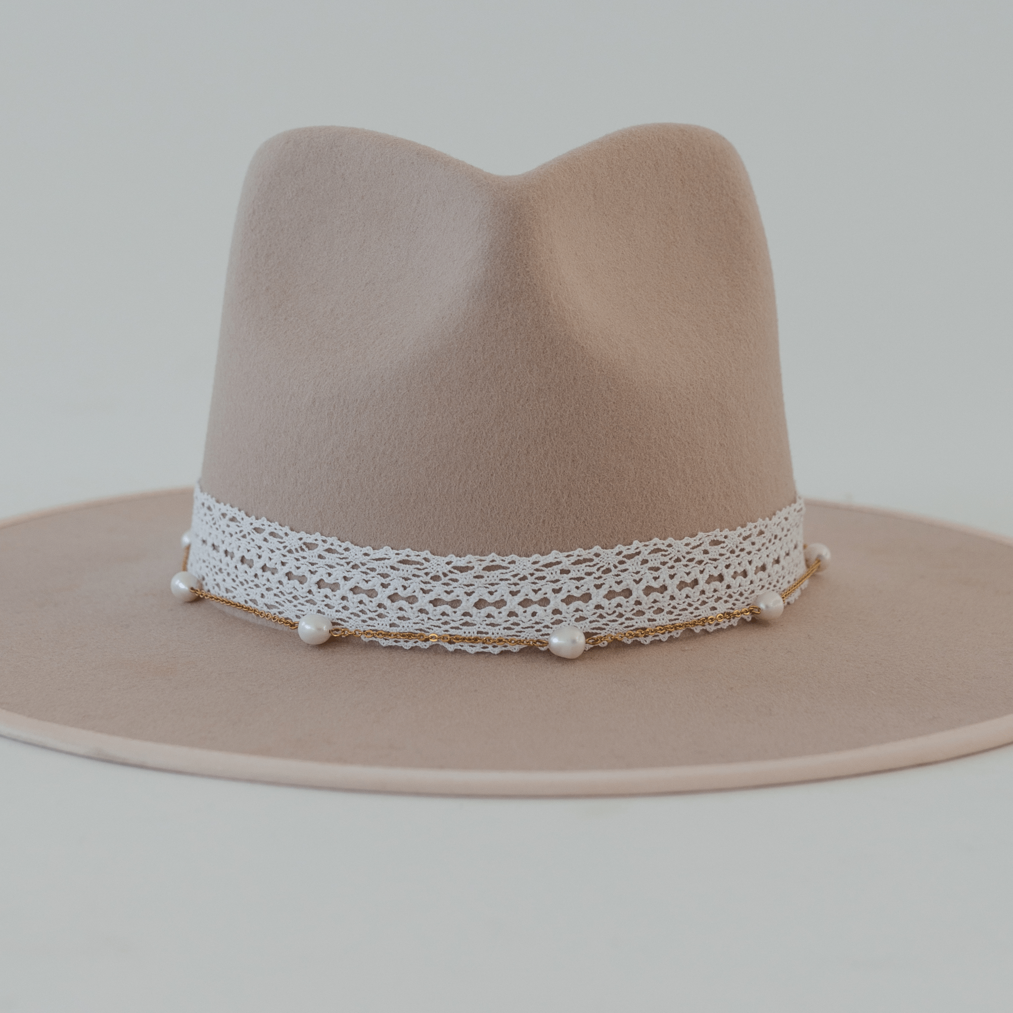 A cream hat with a white lace band and a gold chain with beads against a plain background #color_white