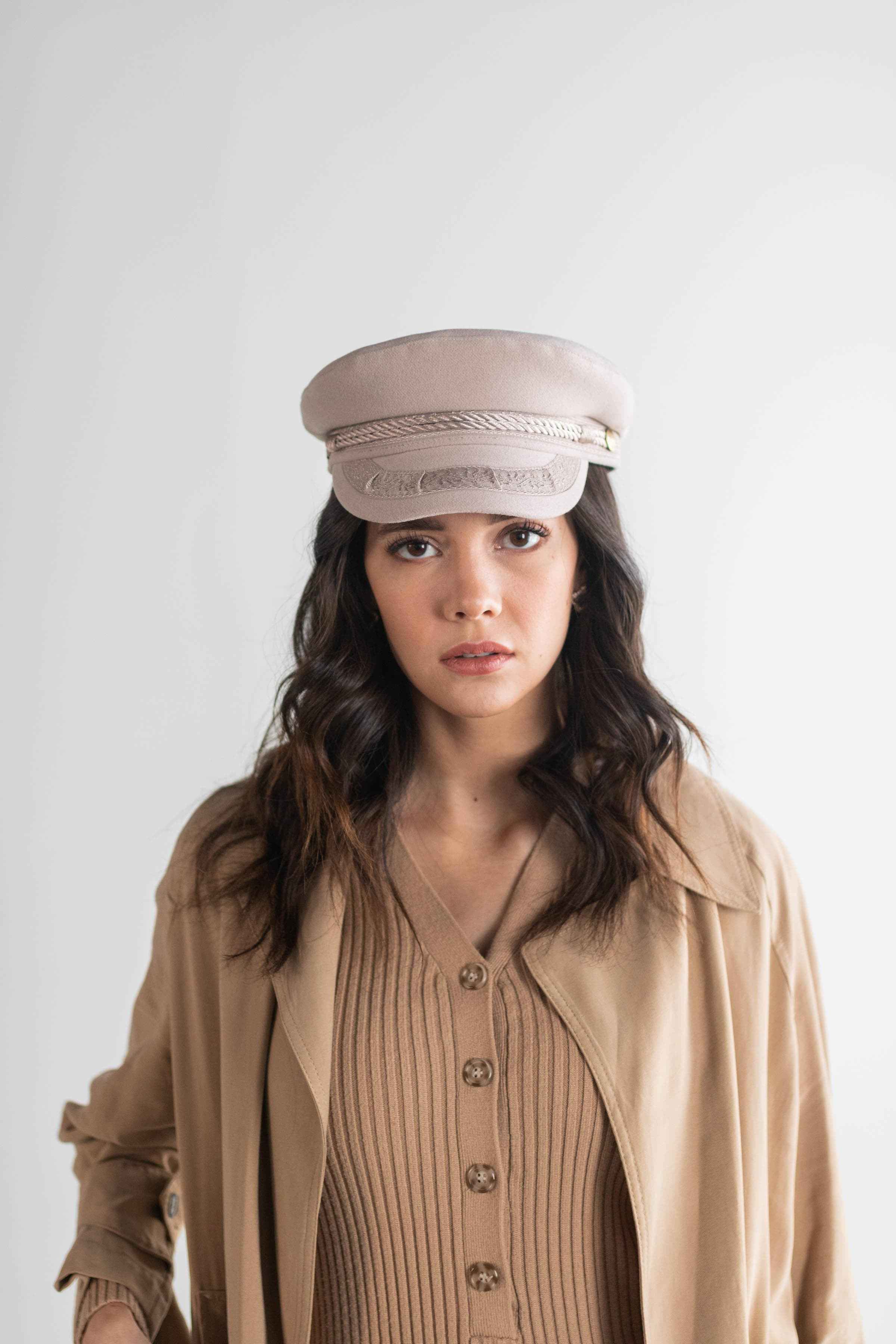 Woman wearing an ivory colored lieutenant cap and a brown shirt with a brown jacket against a plain background #color_ivory