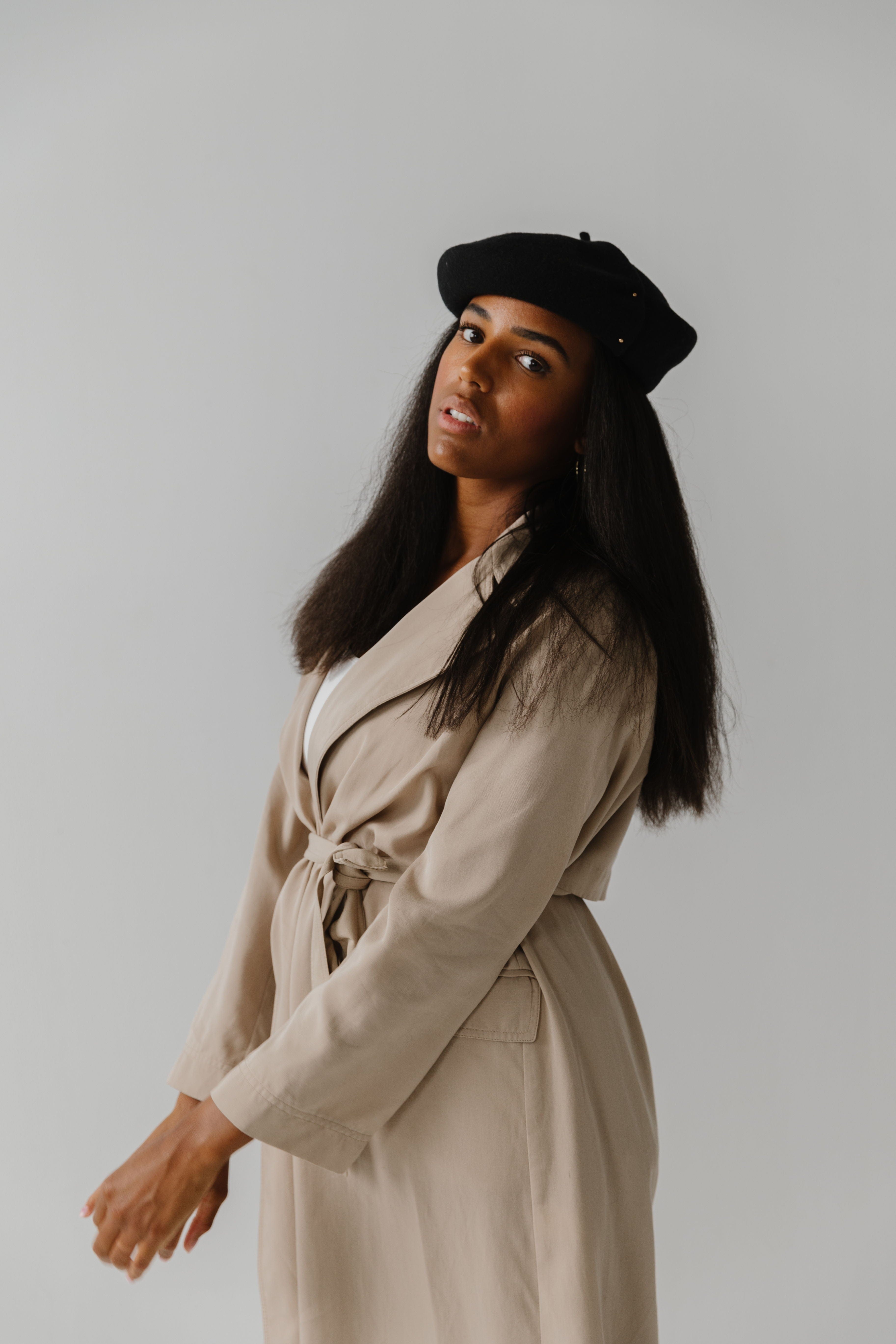 Woman wearing a black beret and a beige coat against a plain background #color_black