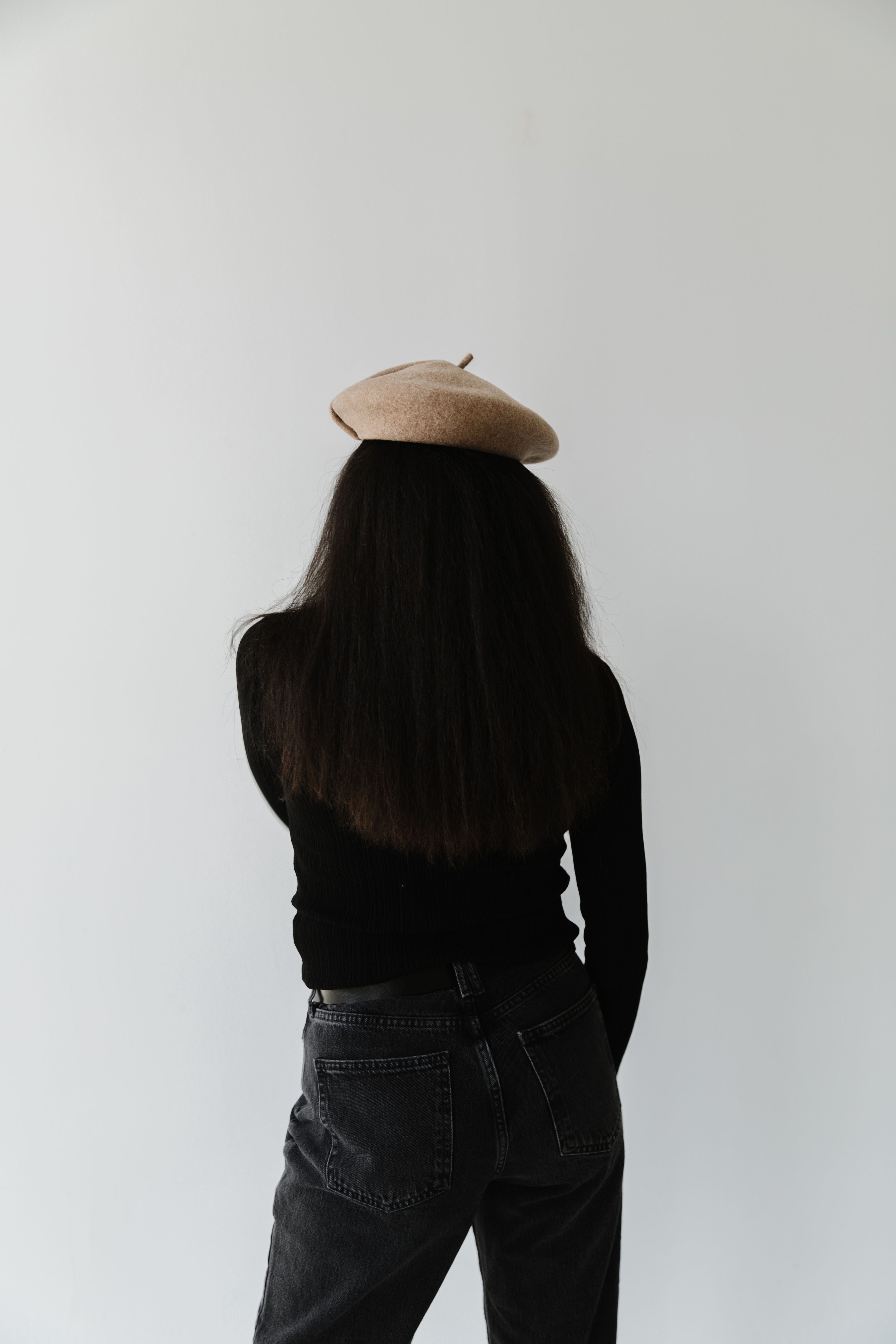 Woman wearing a camel colored beret, a black t-shirt and jeans against a plain background #color_camel
