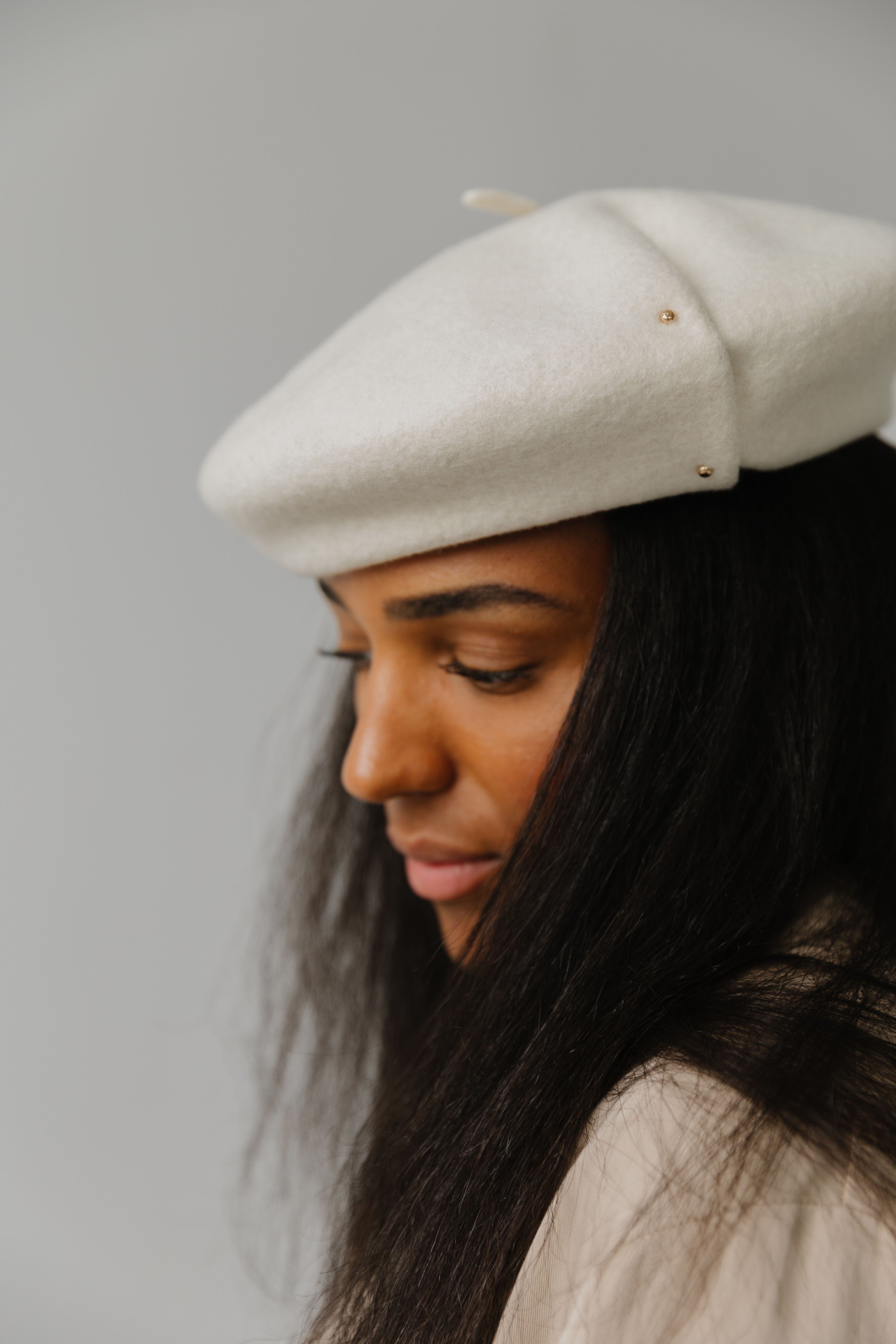 Woman wearing an off white beret facing sideways against a plain background #color_off white