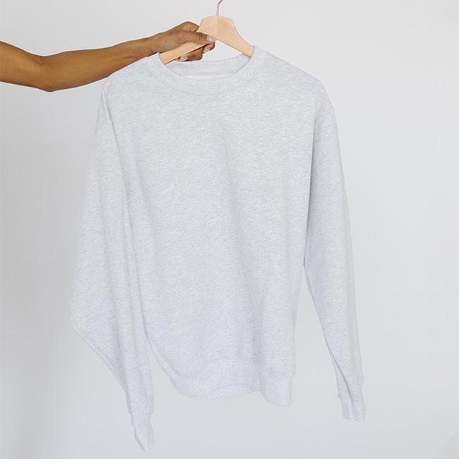 Person carrying an ash colored sweatshirt with the text 'GIGI PIP' in white against a plain background #color_ash-white