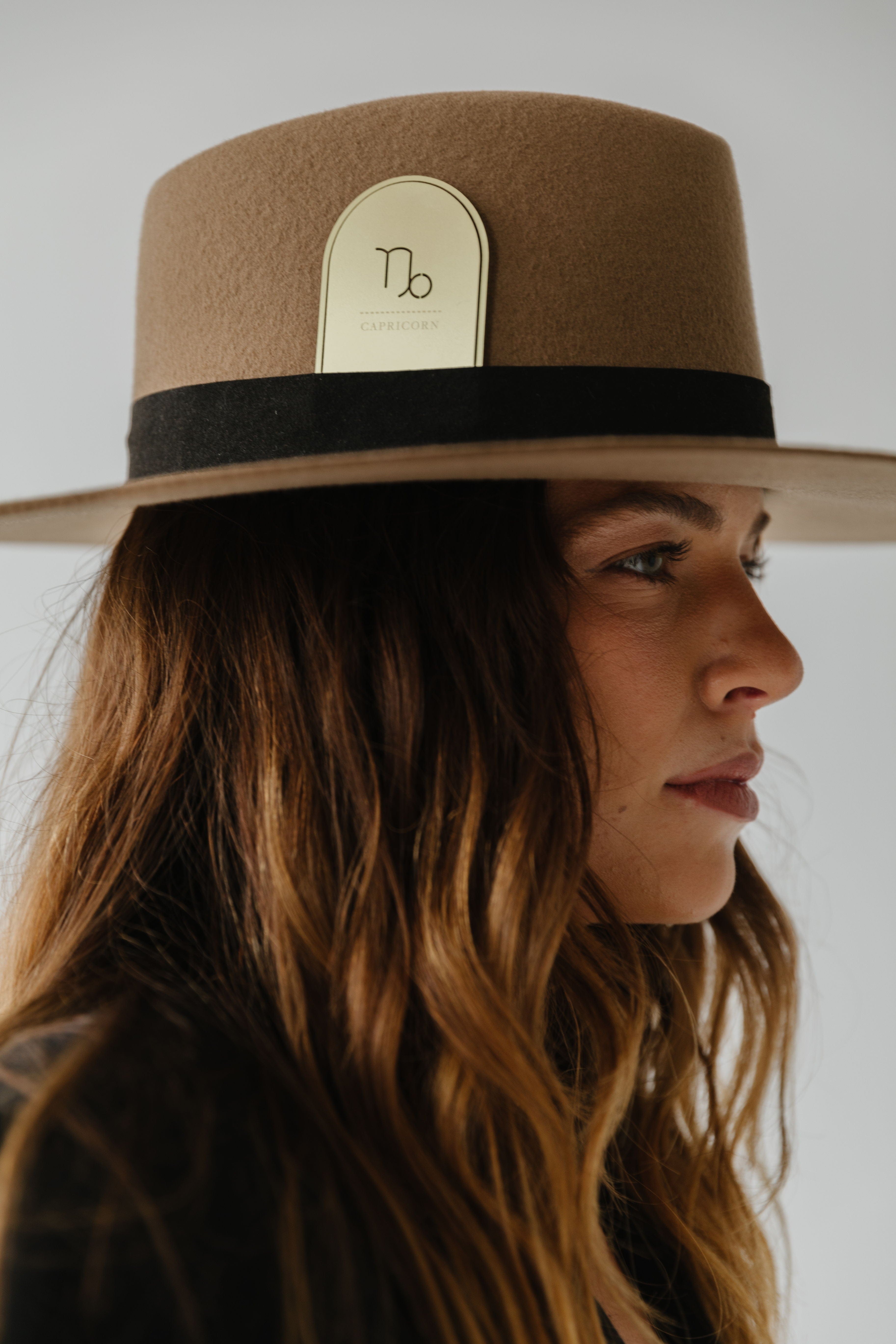 Woman wearing a brown hat with a black band and a gold 'Capricorn' zodiac band card against a plain background #color_gold