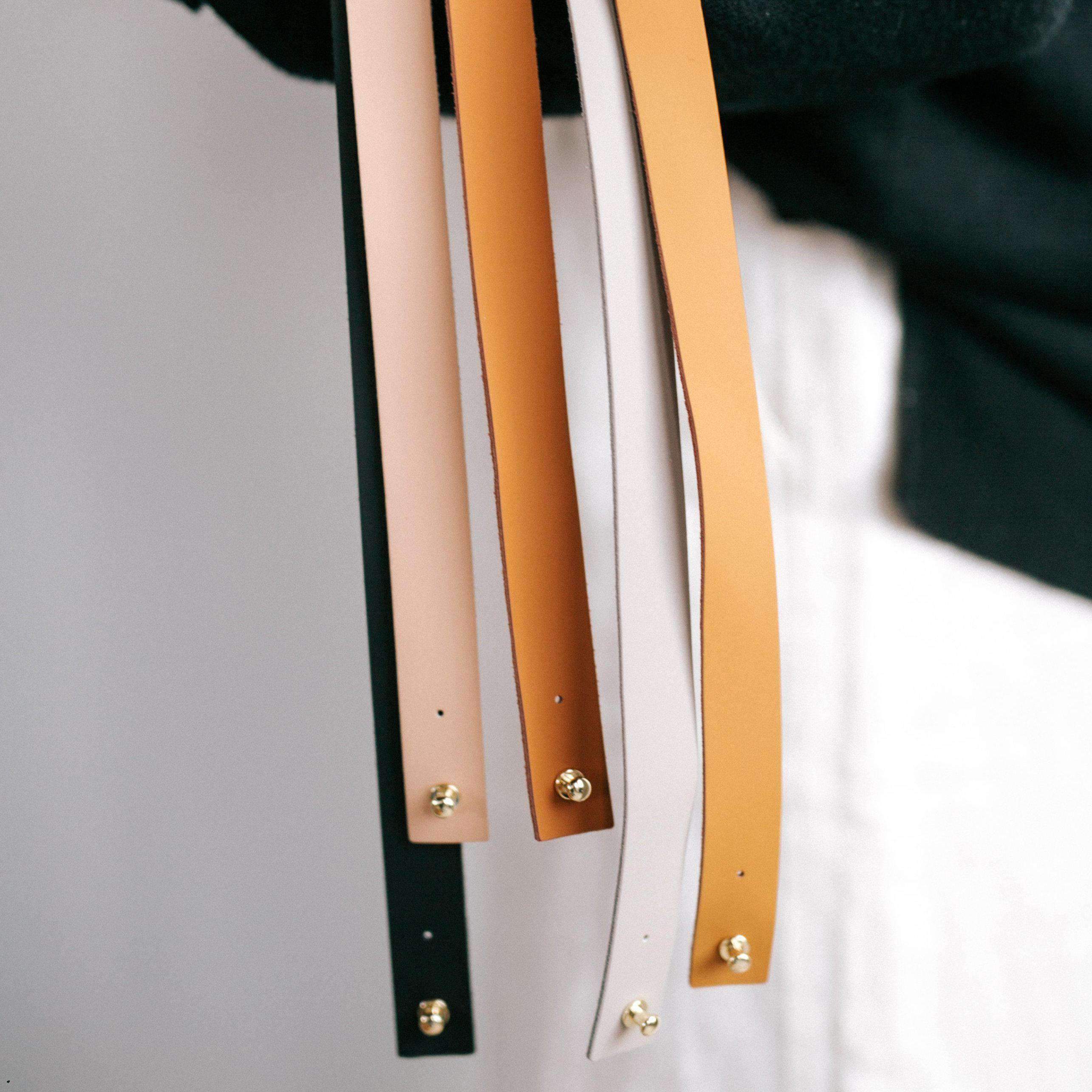 Close up image of black, nude, camel, cognac and stone colored leather bands with pins against a plain background
