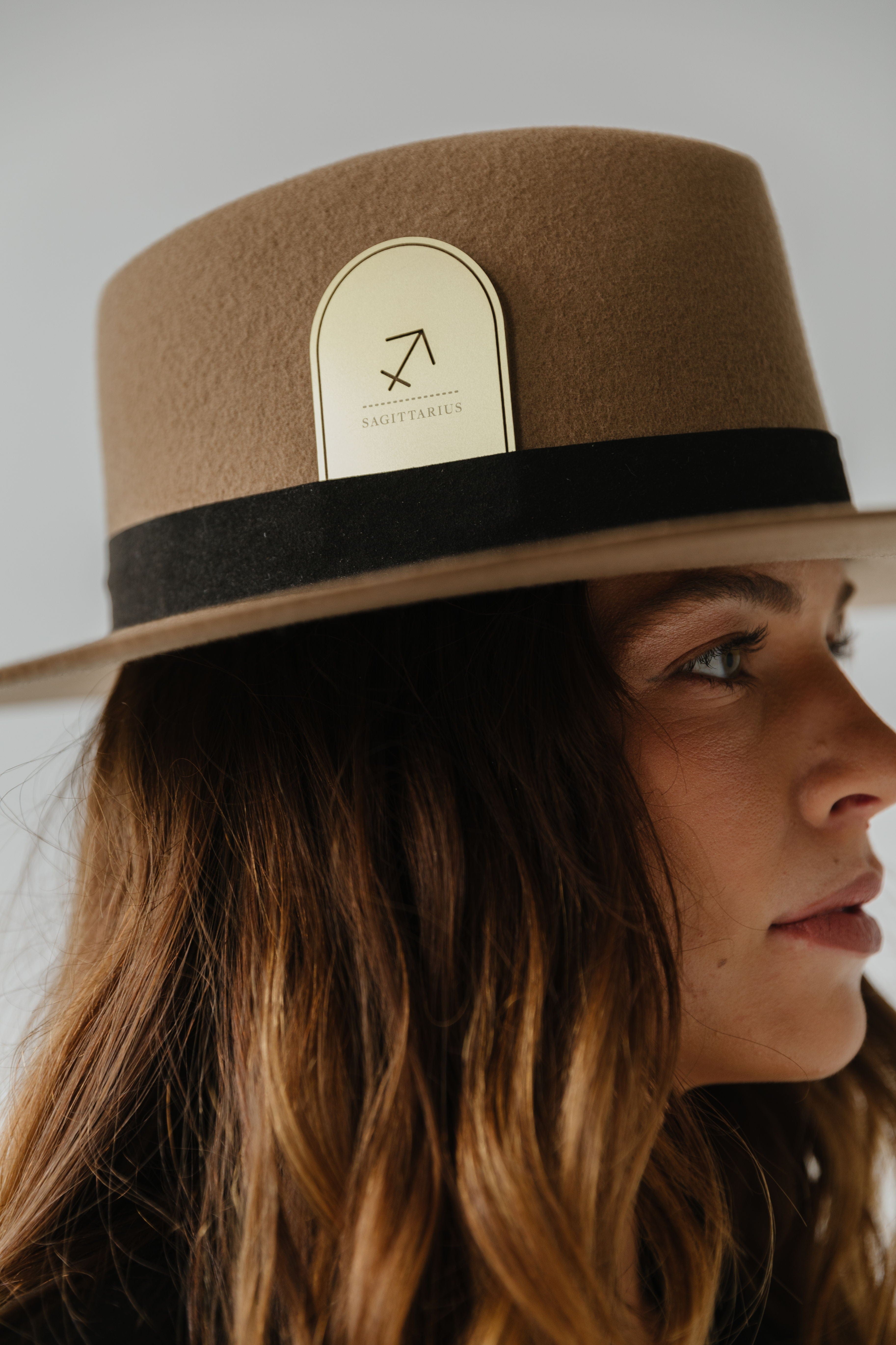 Woman wearing a brown hat with a black band and a gold 'Sagittarius' zodiac band card against a plain background #color_gold
