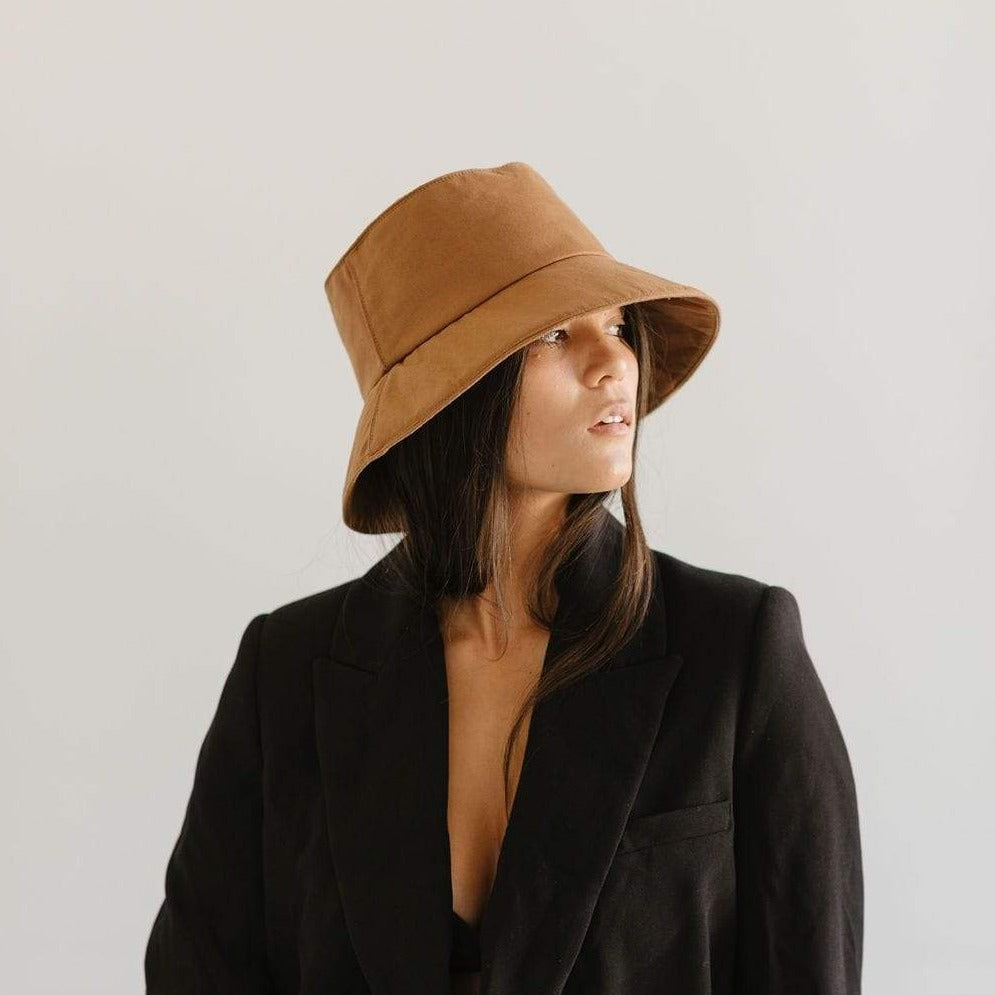Woman wearing a brown packable bucket hat and a black blazer against a plain background #color_brown