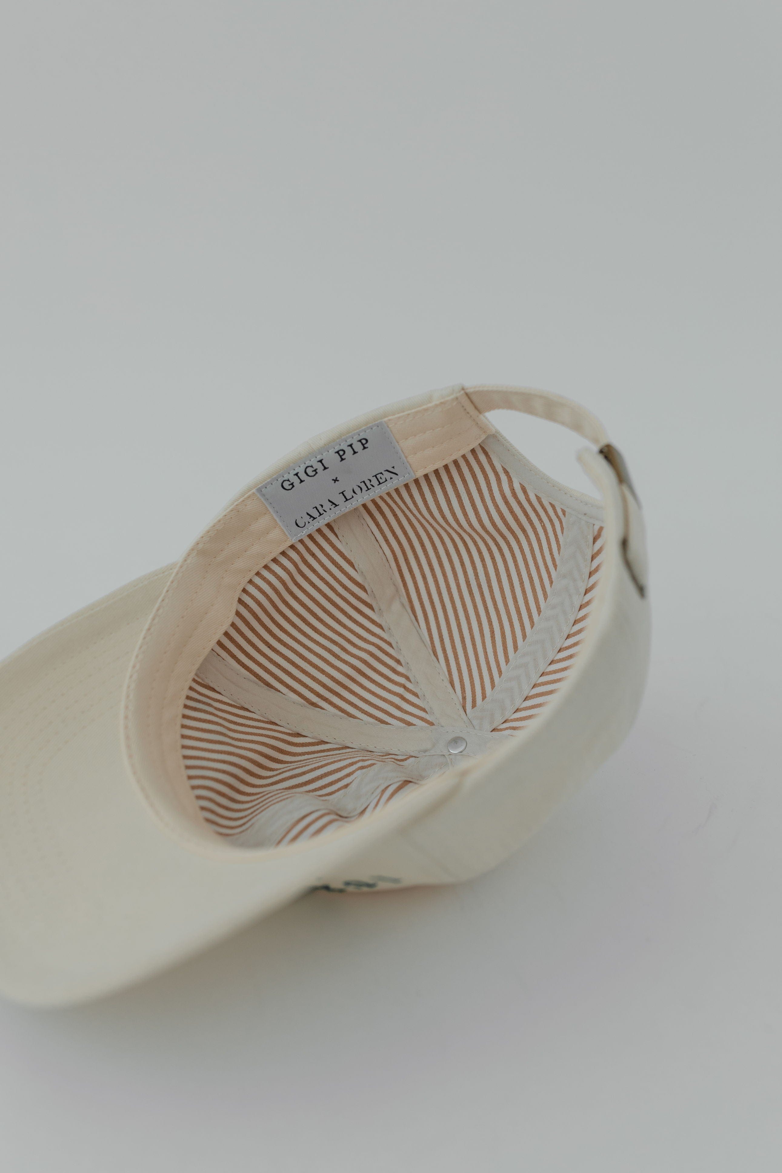 A cream ball cap with the brand label, upside down on a plain background #color_cream