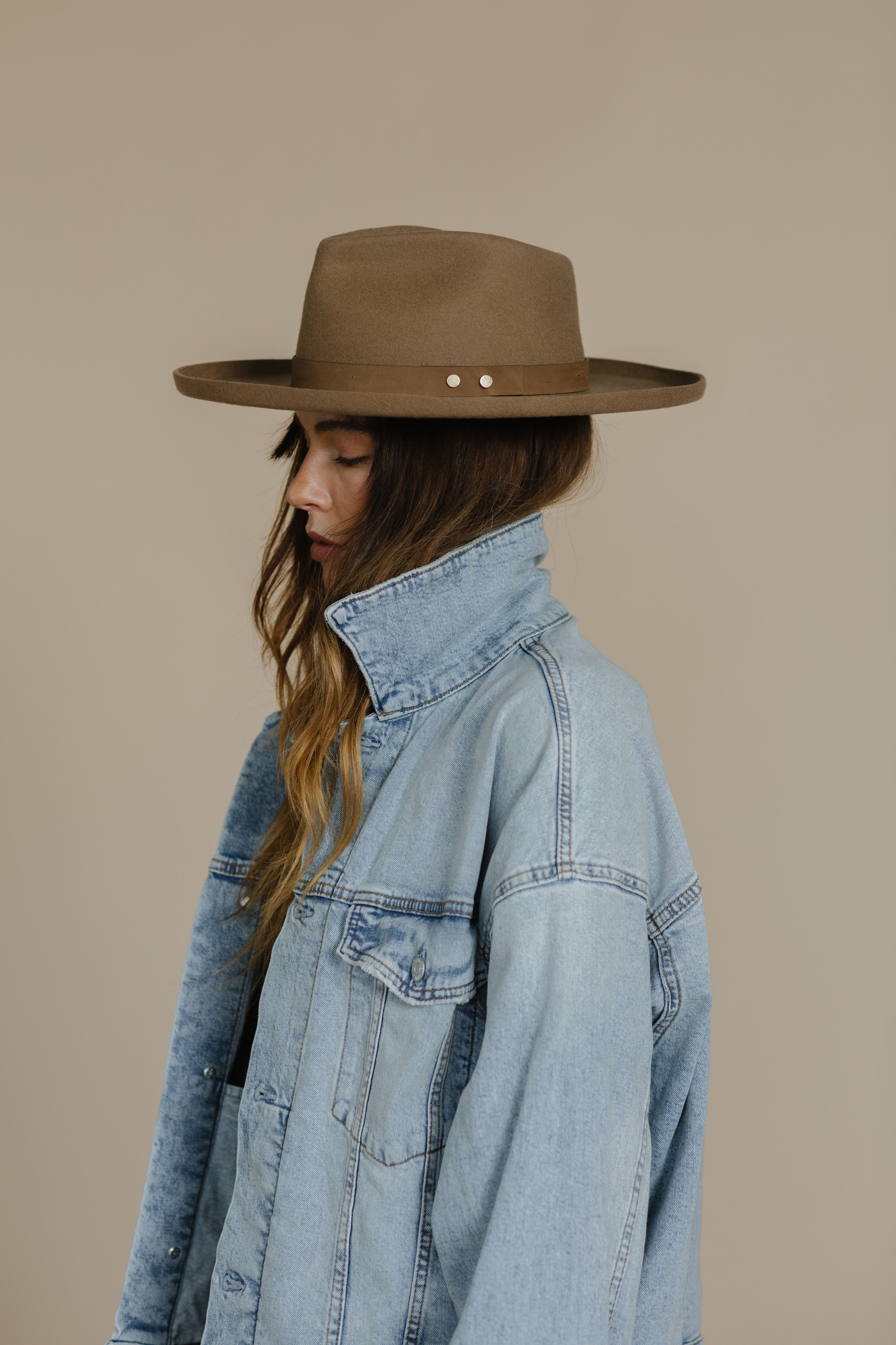 Woman wearing a tan pencil brim fedora hat with a hat band and a denim jacket, facing sideways against a plain background #color_tan