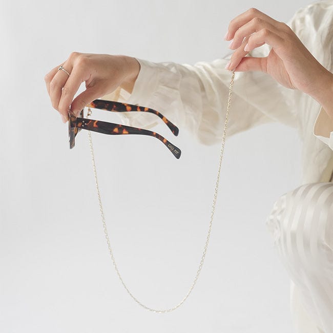 Sunglasses with a gold chain strap being held by a person wearing a white shirt against a plain background #color_gold