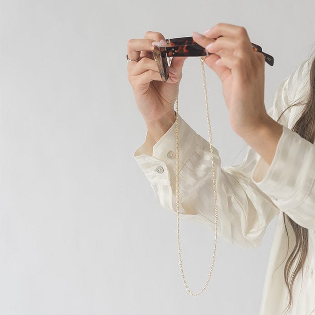 Sunglasses with a gold chain strap being held by a person against a plain background #color_gold