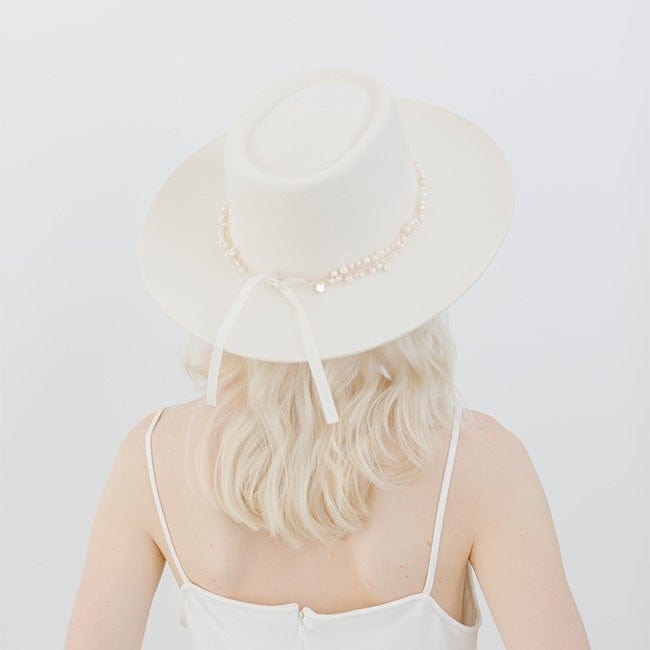 Woman wearing a white hat with a gold decorative band with beads and a white top, facing behind against a plain background #color_gold