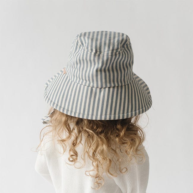 Young girl wearing a blue and white striped bucket hat and a white shirt, facing behind against a plain background #color_striped-blue