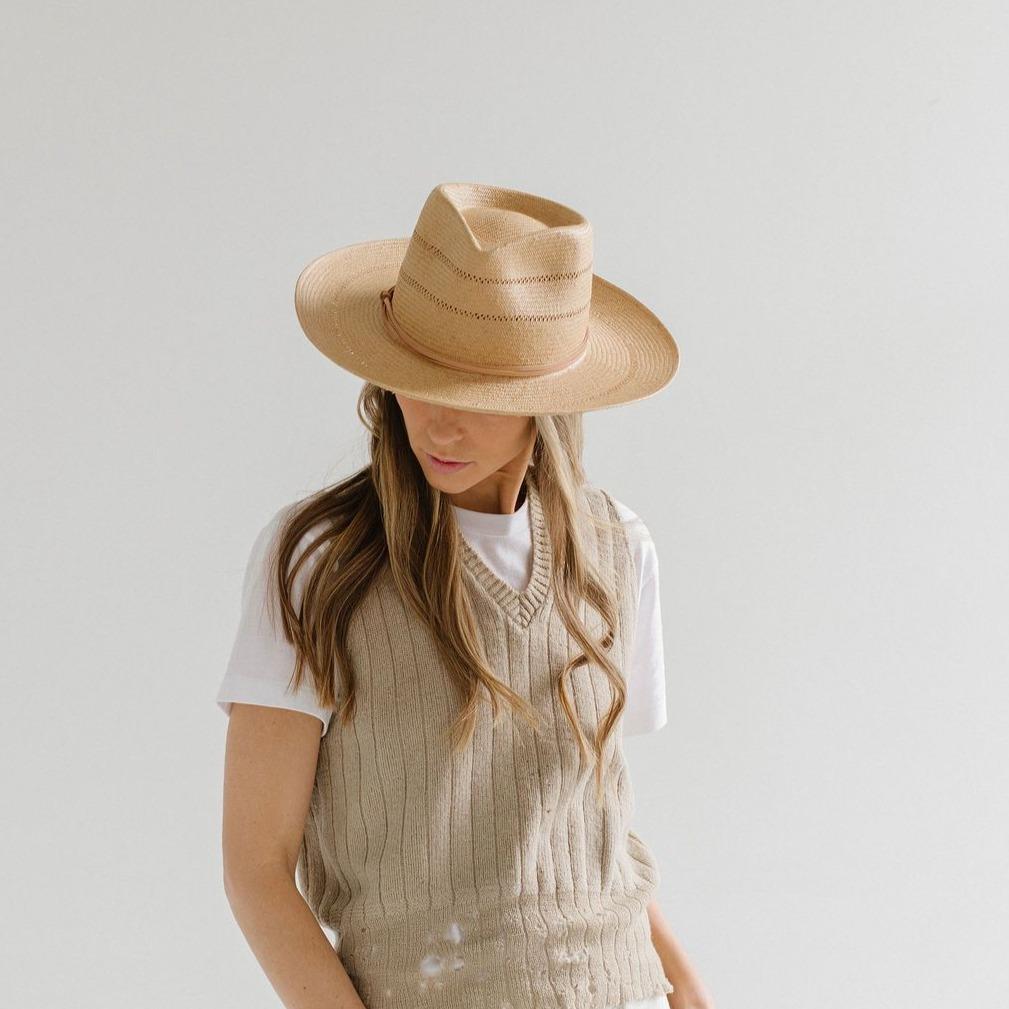 Woman wearing a honey colored fedora straw hat with a hat band and a beige sweater against a plain background #color_honey