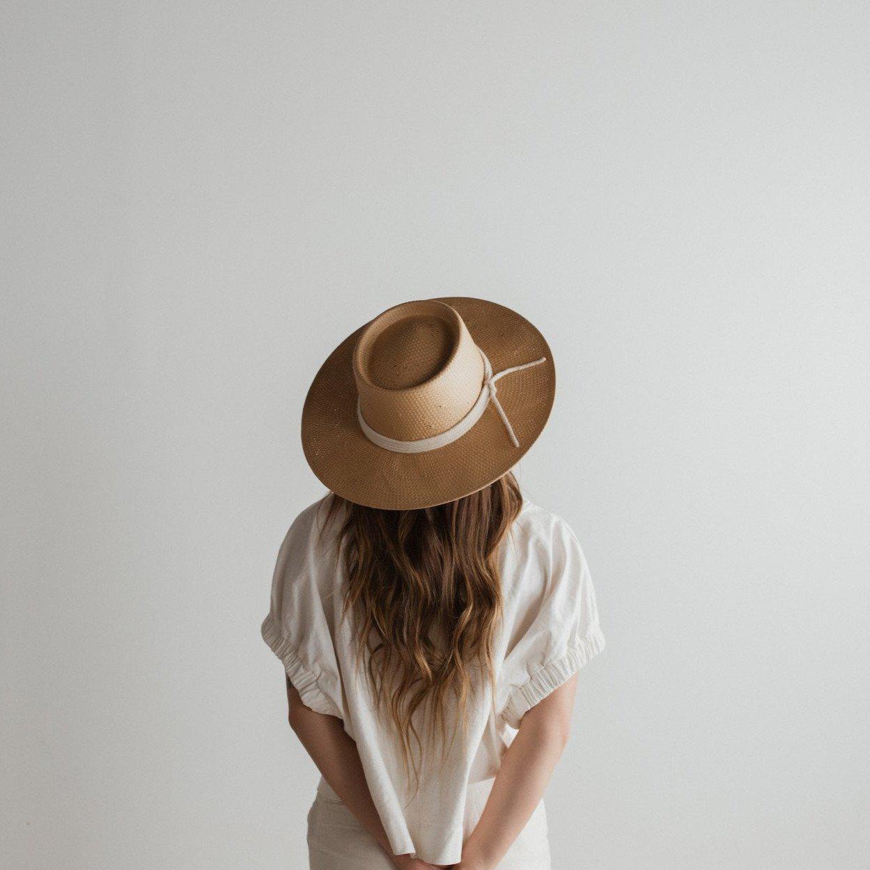 Woman wearing a natural colored straw hat with a white rope hat band and a white top, facing behind against a plain background #color_natural