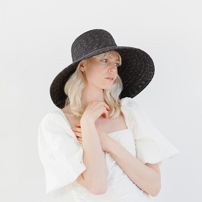 Woman wearing a black boater-style straw hat and a white top, looking sideways against a plain background #color_black
