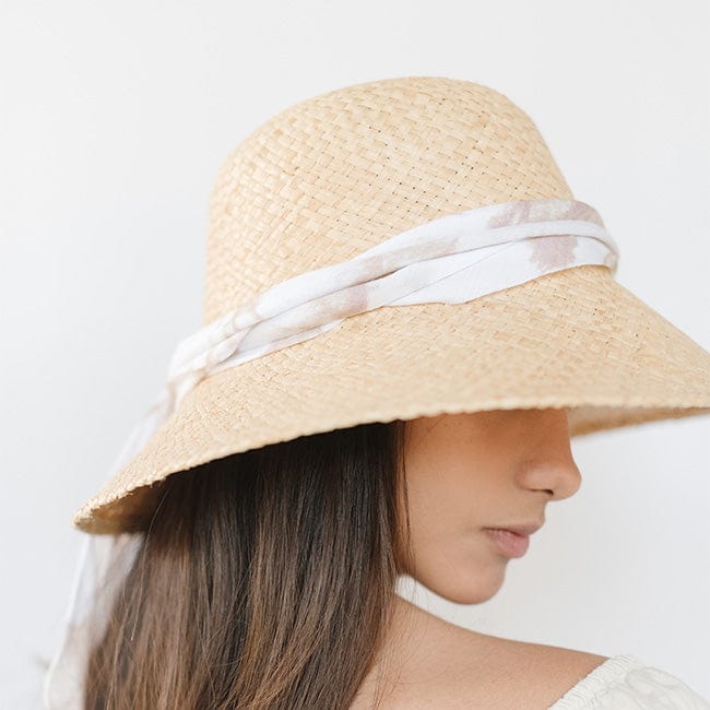 Woman wearing a natural colored packable straw hat with a band facing sideways against a plain background #color_natural