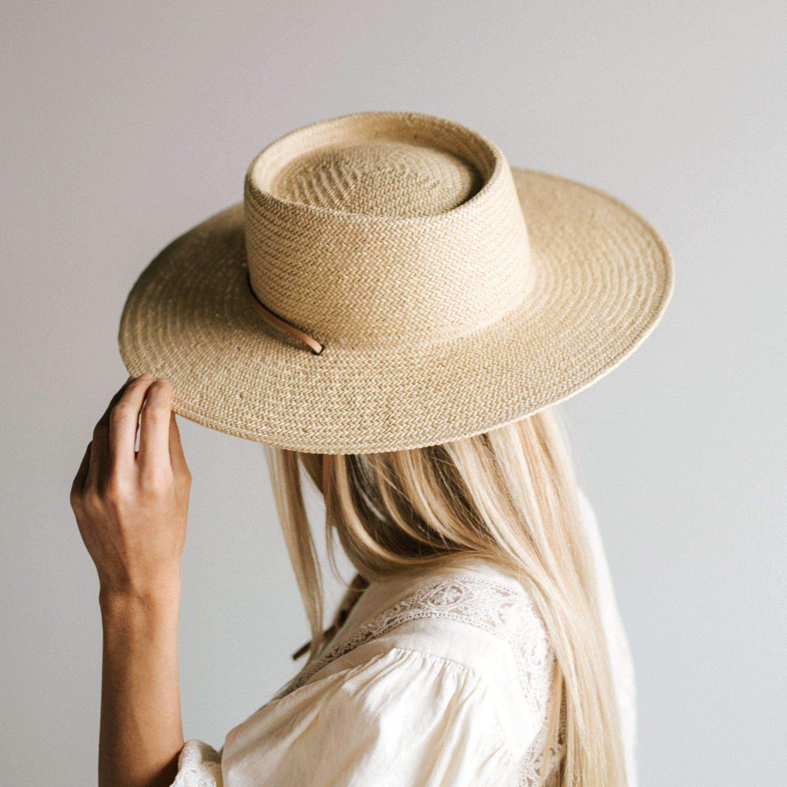 Woman wearing a cream straw hat with a band and a white top, looking behind against a plain background #color_cream