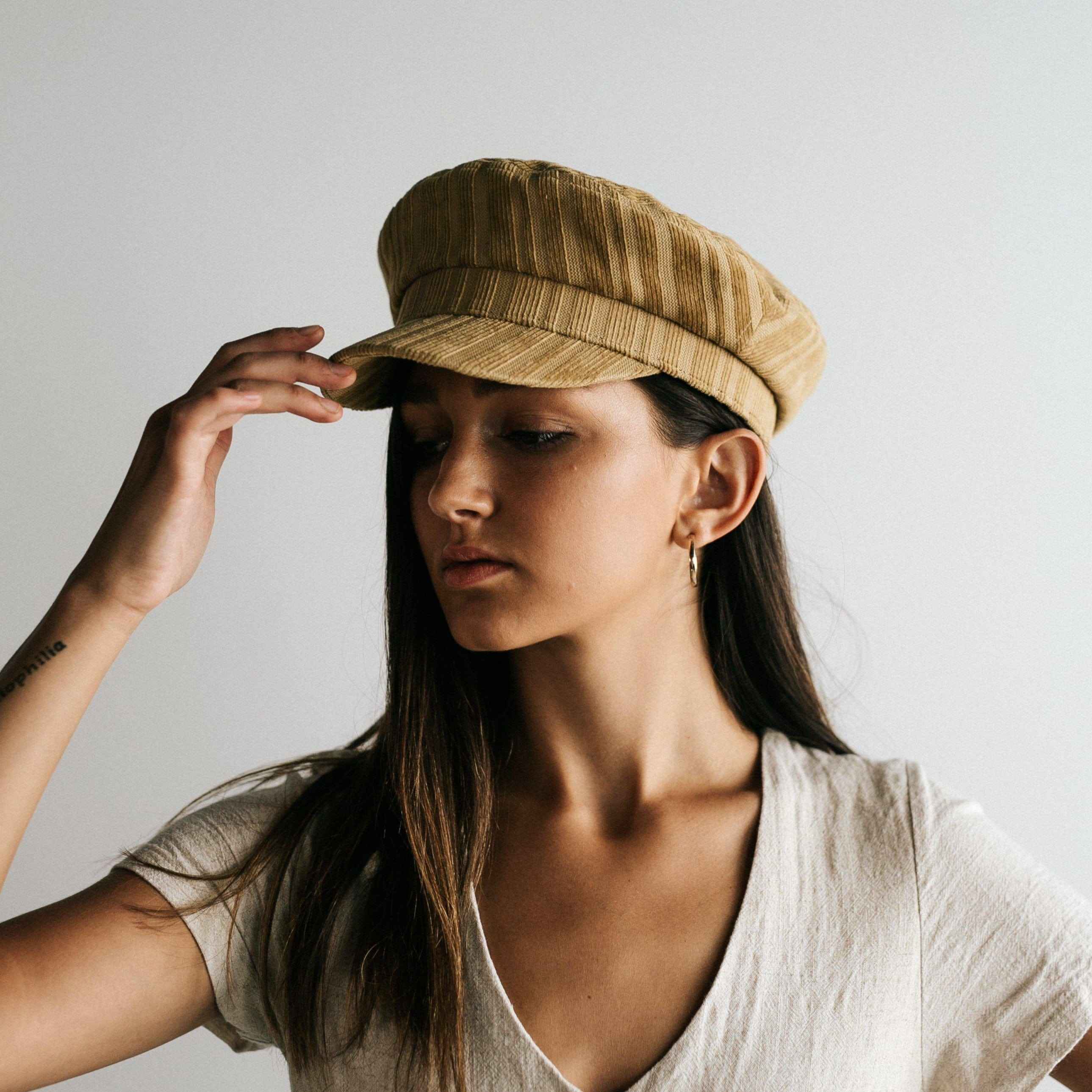 Woman wearing a mustard colored striped cap and a white t-shirt against a plain background #color_mustard