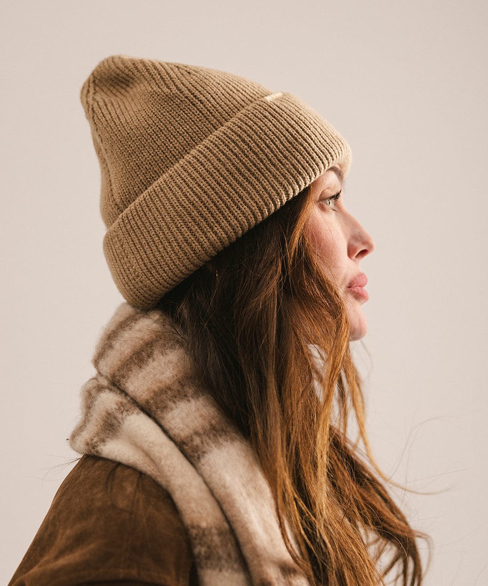 Person wearing a beige knit beanie and a fur-lined scarf on a plain background #color_tan