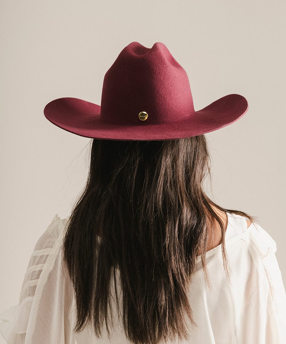 Woman wearing a merlot colored cowboy hat and a white shirt, facing behind against a plain background #color_merlot