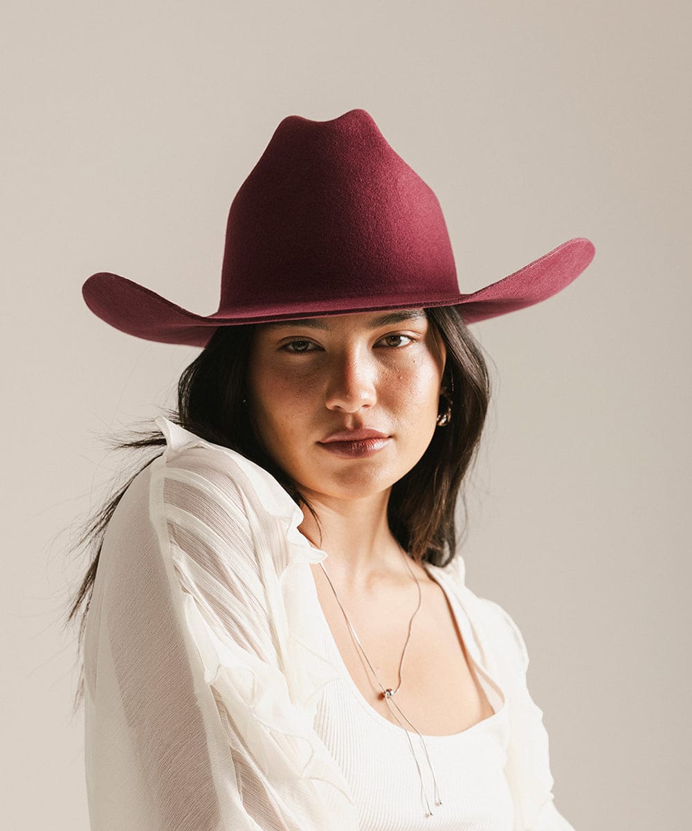 Woman wearing a merlot colored cowboy hat and a white shirt against a plain background #color_merlot