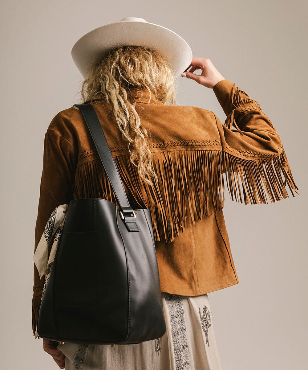 Person wearing a brown fringed jacket and white hat, holding a black bag. #color_black
