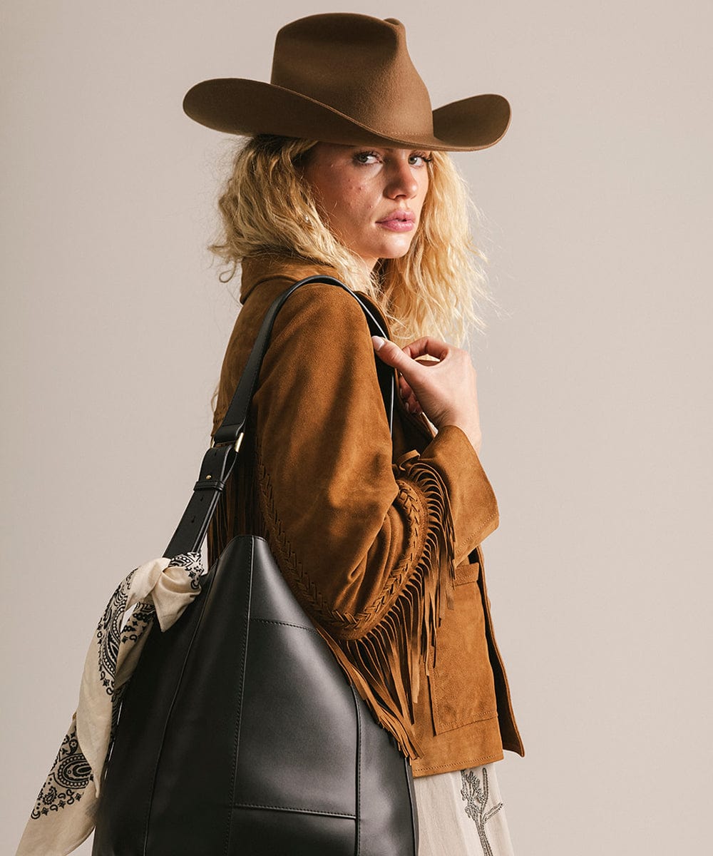 Woman wearing a brown cowboy hat and jacket with a black leather bag on a plain background #color_black