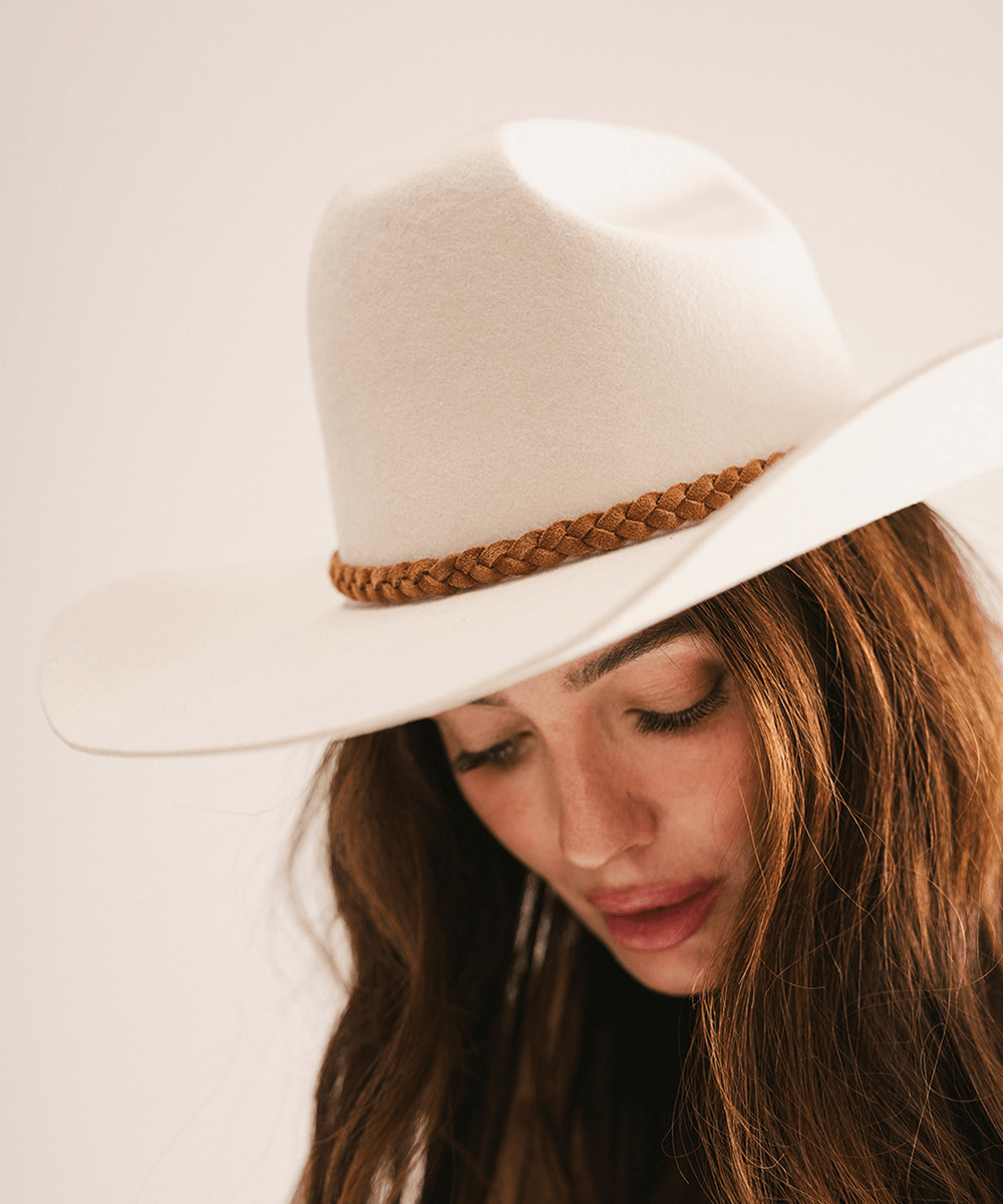 Woman wearing a white cowboy hat with a brown band on a plain background #color_caramel