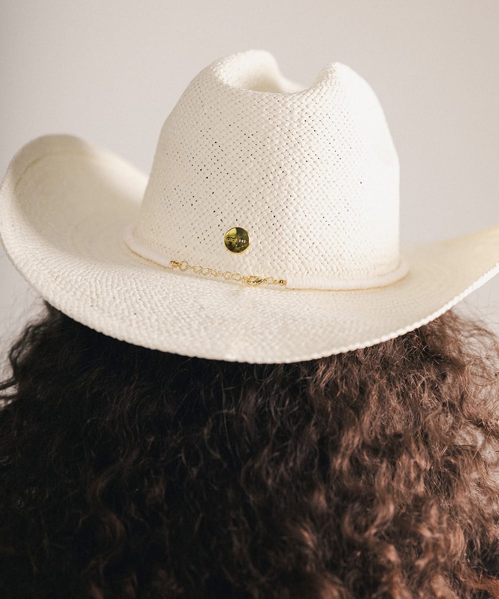 White cowboy hat with a gold band and a decorative band worn by a woman on a plain background #color_cream