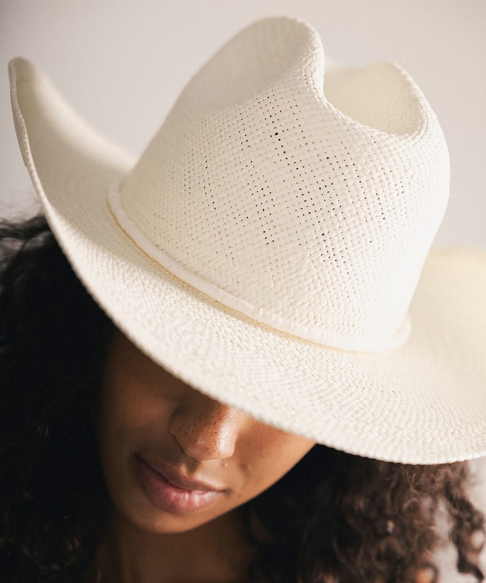 Close-up of a person wearing a white cowboy hat with a decorative band against a plain background #color_cream