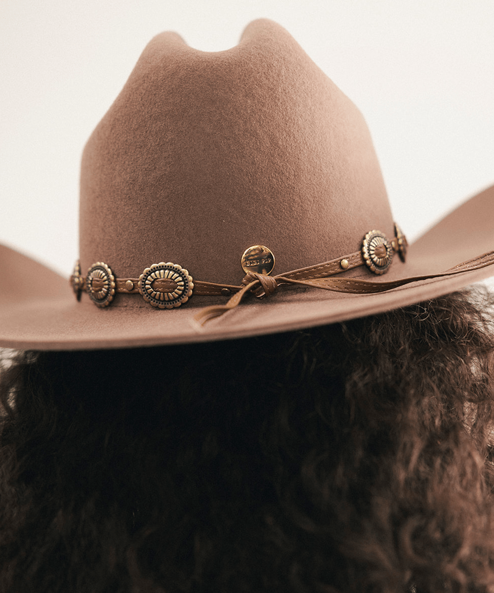 Woman wearing a brown cowboy hat with decorative band against a neutral background #color_chocolate