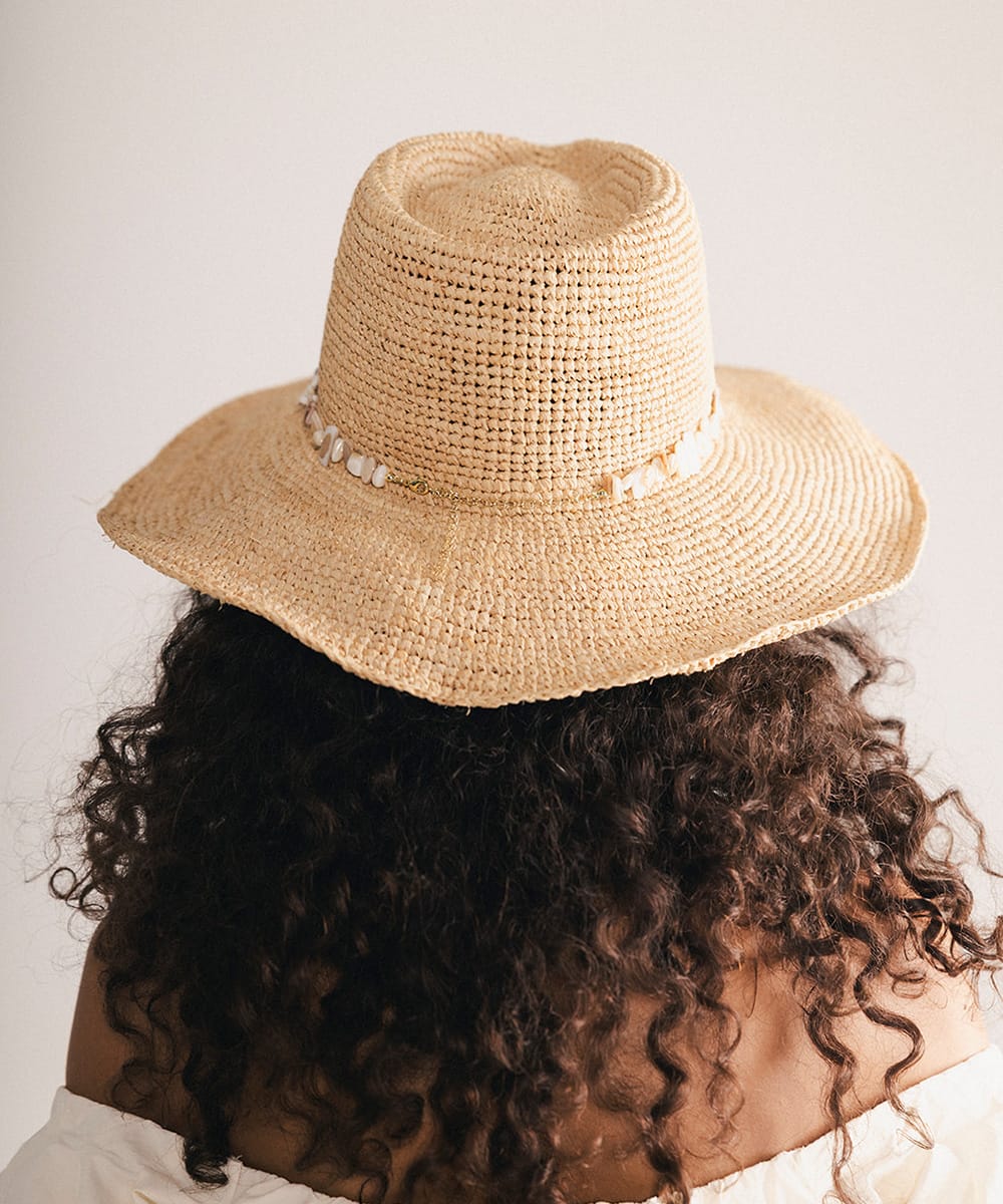 Woman wearing a straw hat with a decorative band in a plain background #color_natural