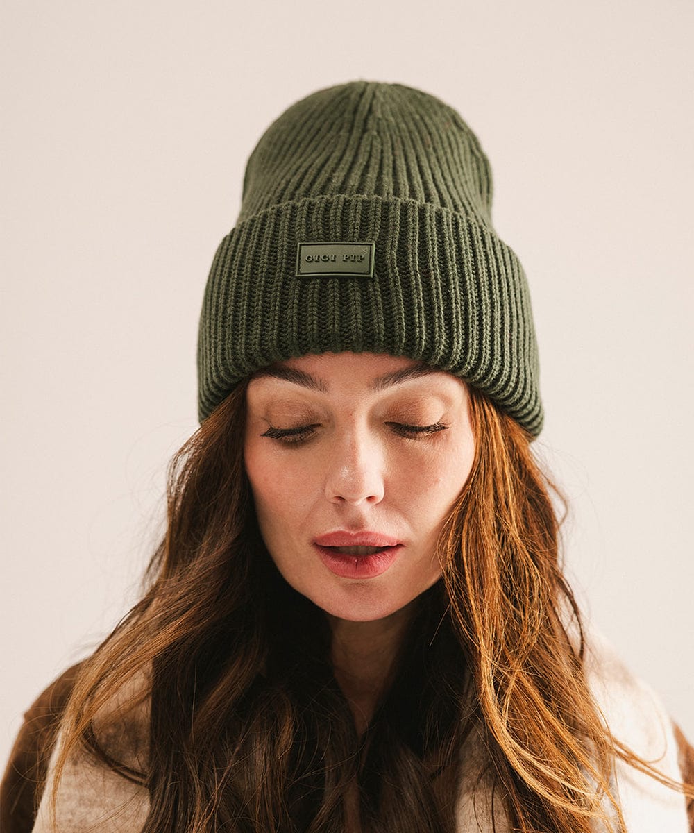 A woman wearing a dark green chunky ribbed beanie against a plain background #color_dark green