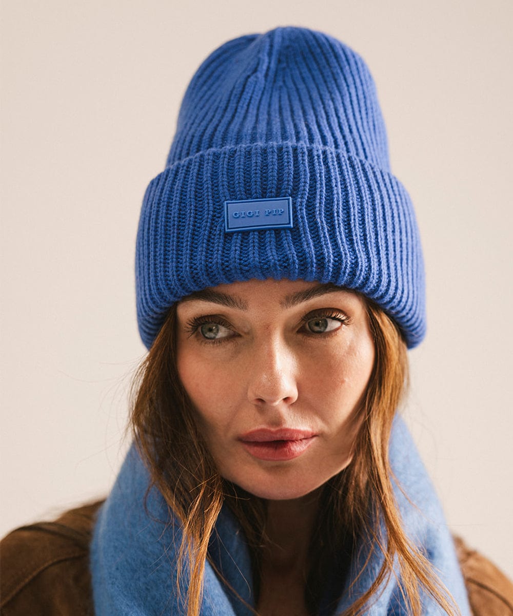 Woman wearing an alpine blue knit beanie and scarf against a beige background #color_alpine blue