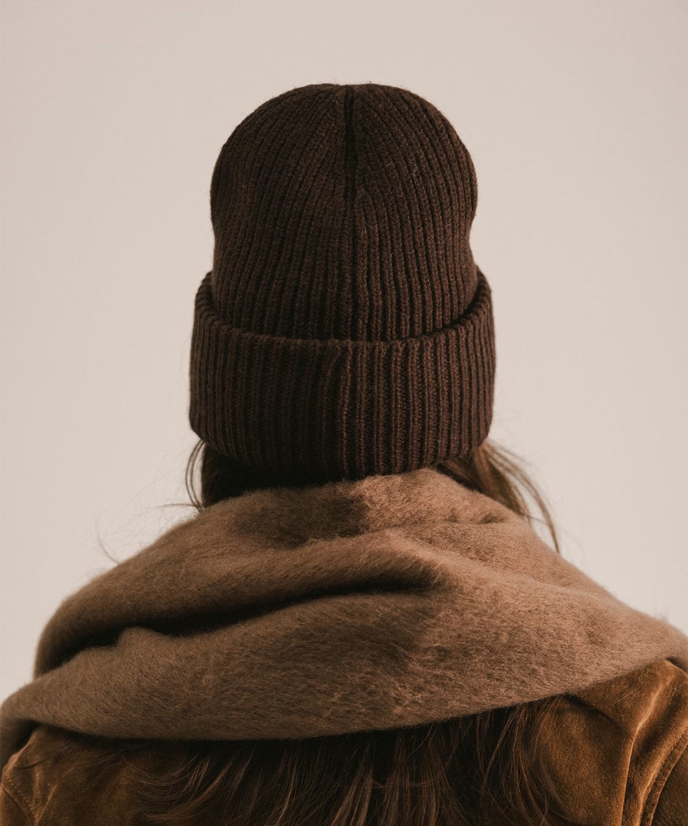 Person wearing a dark brown knit beanie and coat, facing behind against a plain background #color_dark brown