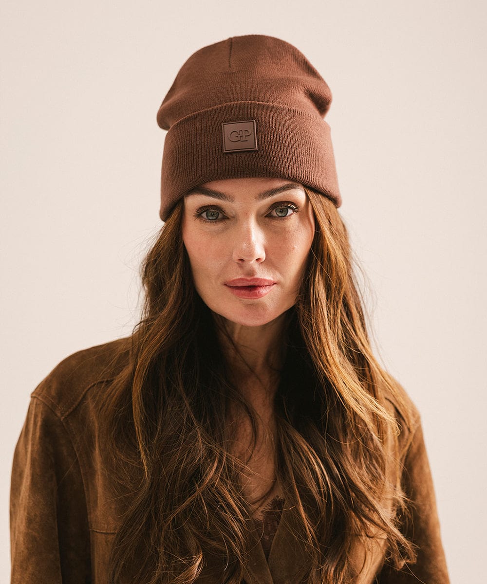 Woman wearing a chocolate colored beanie and brown coat against a plain background #color_chocolate