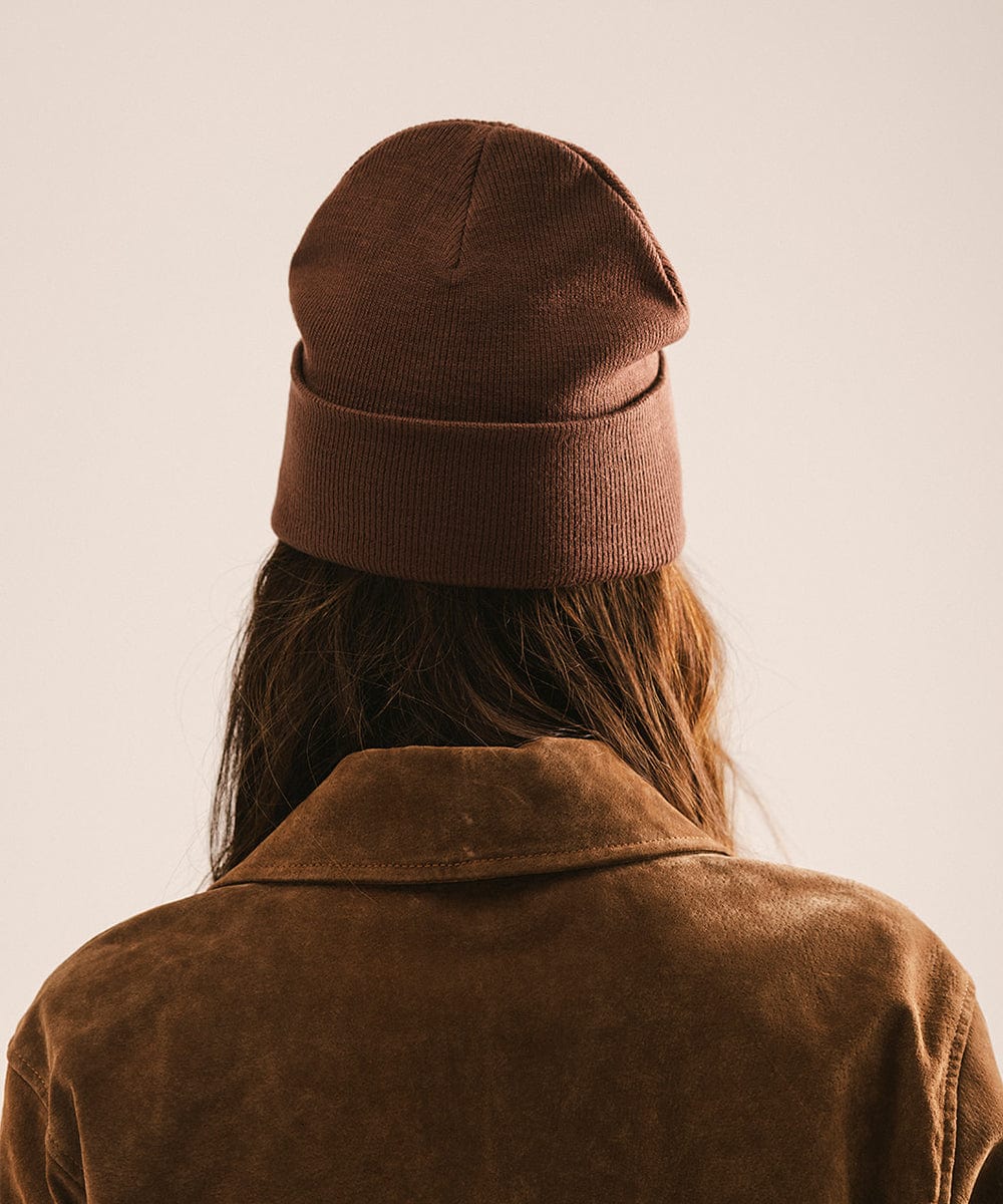 Person wearing a chocolate colored beanie and brown jacket, facing behind against a plain background #color_chocolate