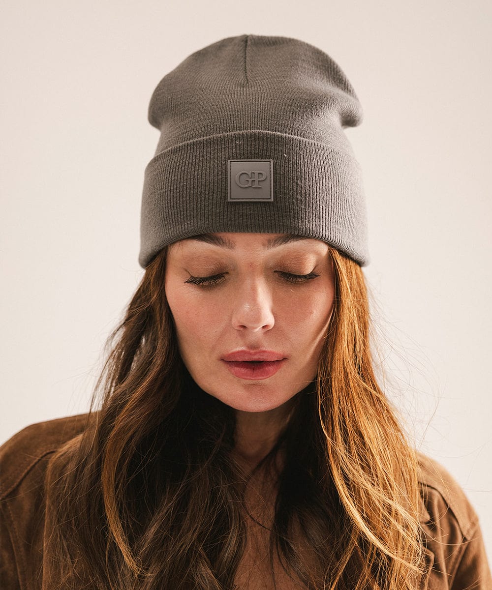 Woman wearing a grey beanie with a logo on a plain background #color_grey