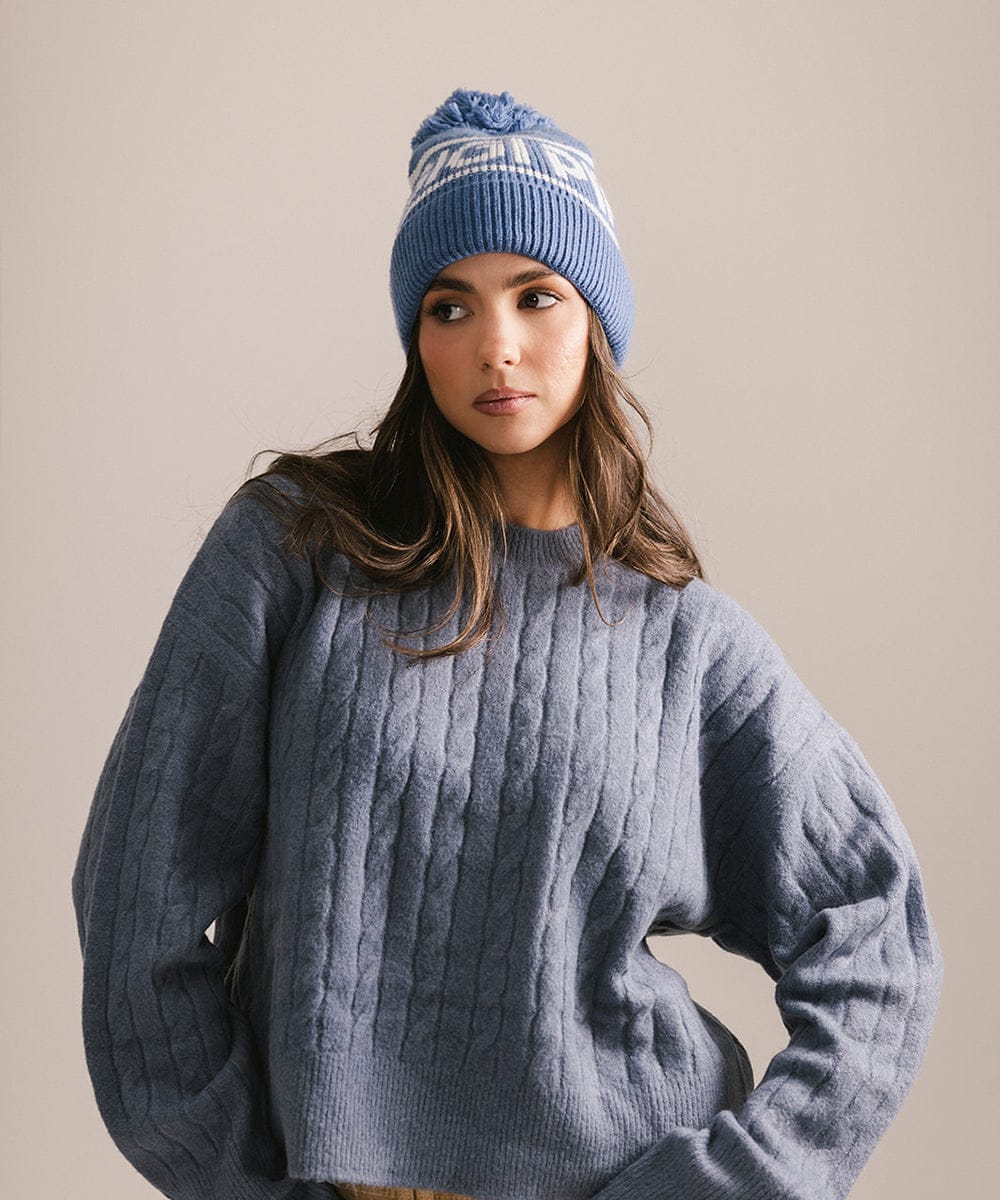 Woman wearing a blue knit beanie and gray sweater against a beige background #color_arctic blue