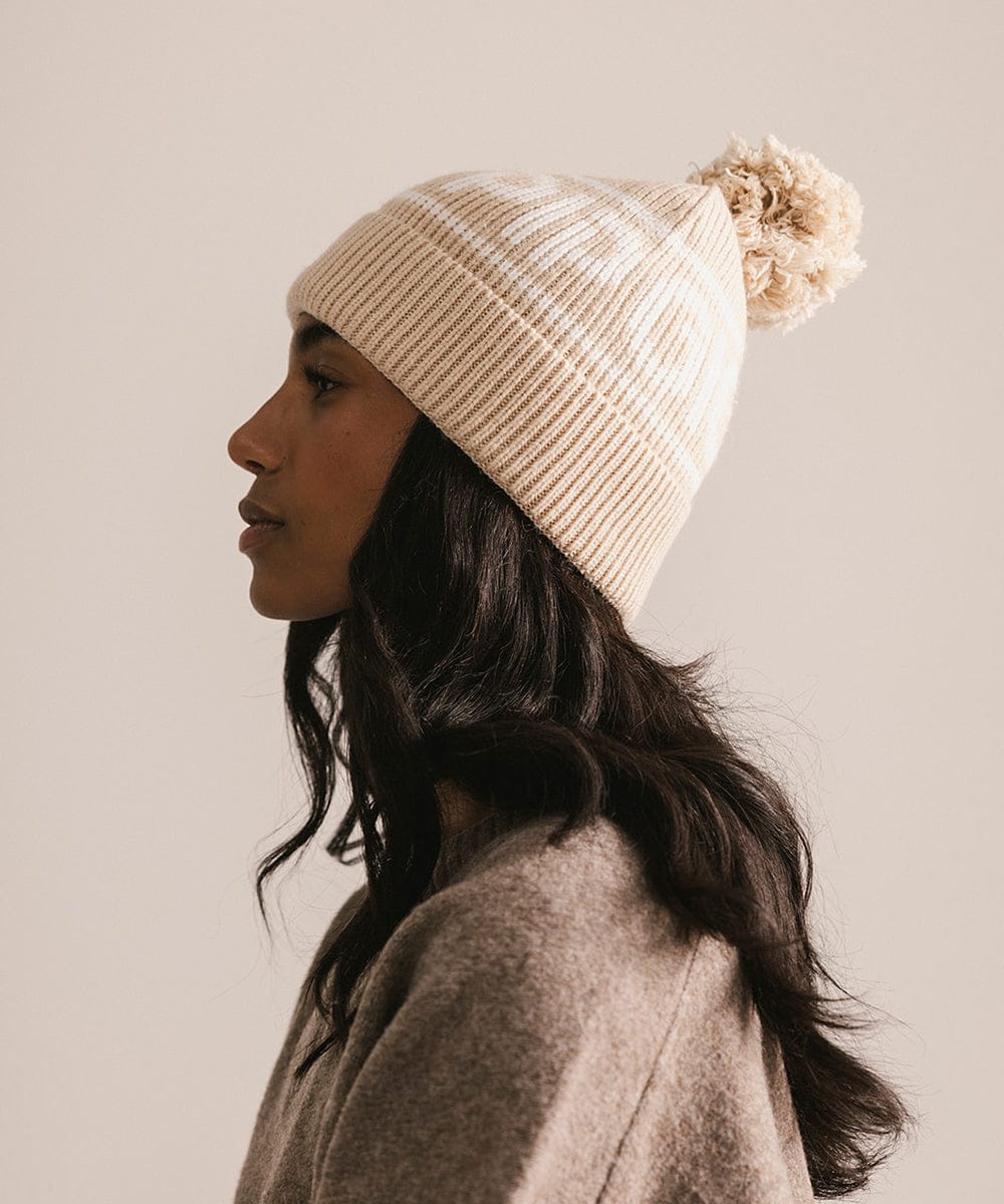 Woman wearing a beige knitted beanie with a pom-pom on a plain background #color_taupe